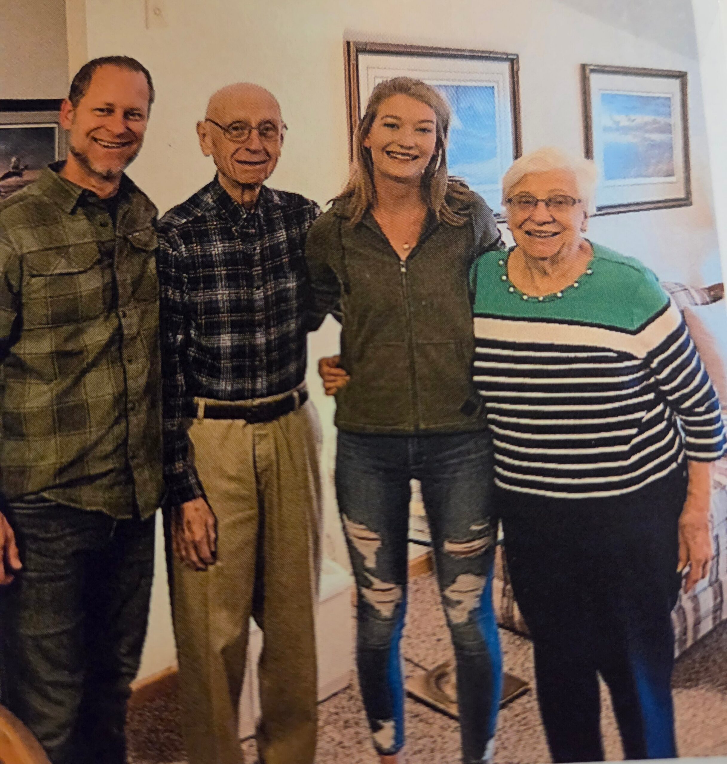 Four adults stand side by side indoors, smiling at the camera with framed art on the wall behind them.