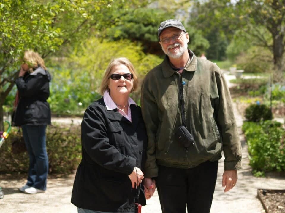 Smiling older couple holding hands on a sunny garden path in a park.