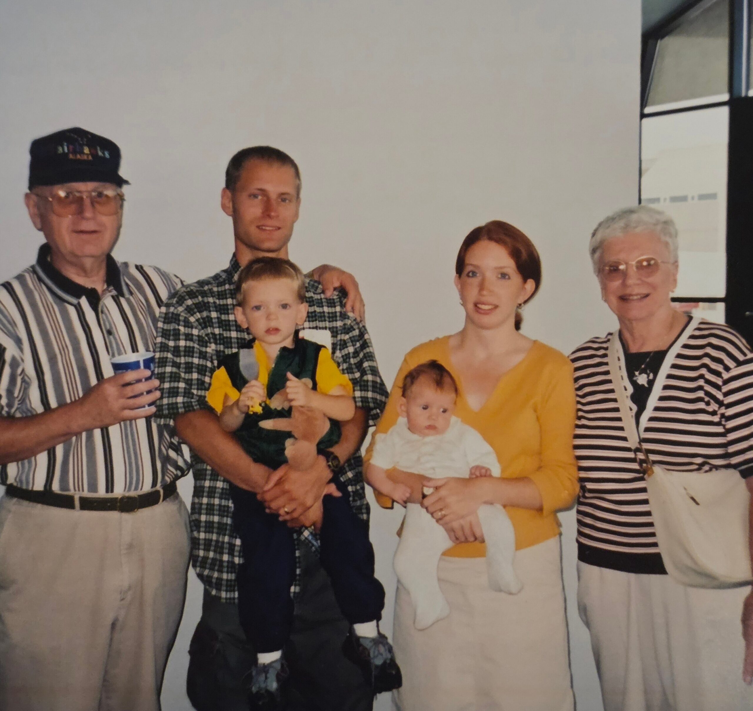A family portrait of several adults and children standing together, posing for the camera in matching casual outfits in a studio setting.