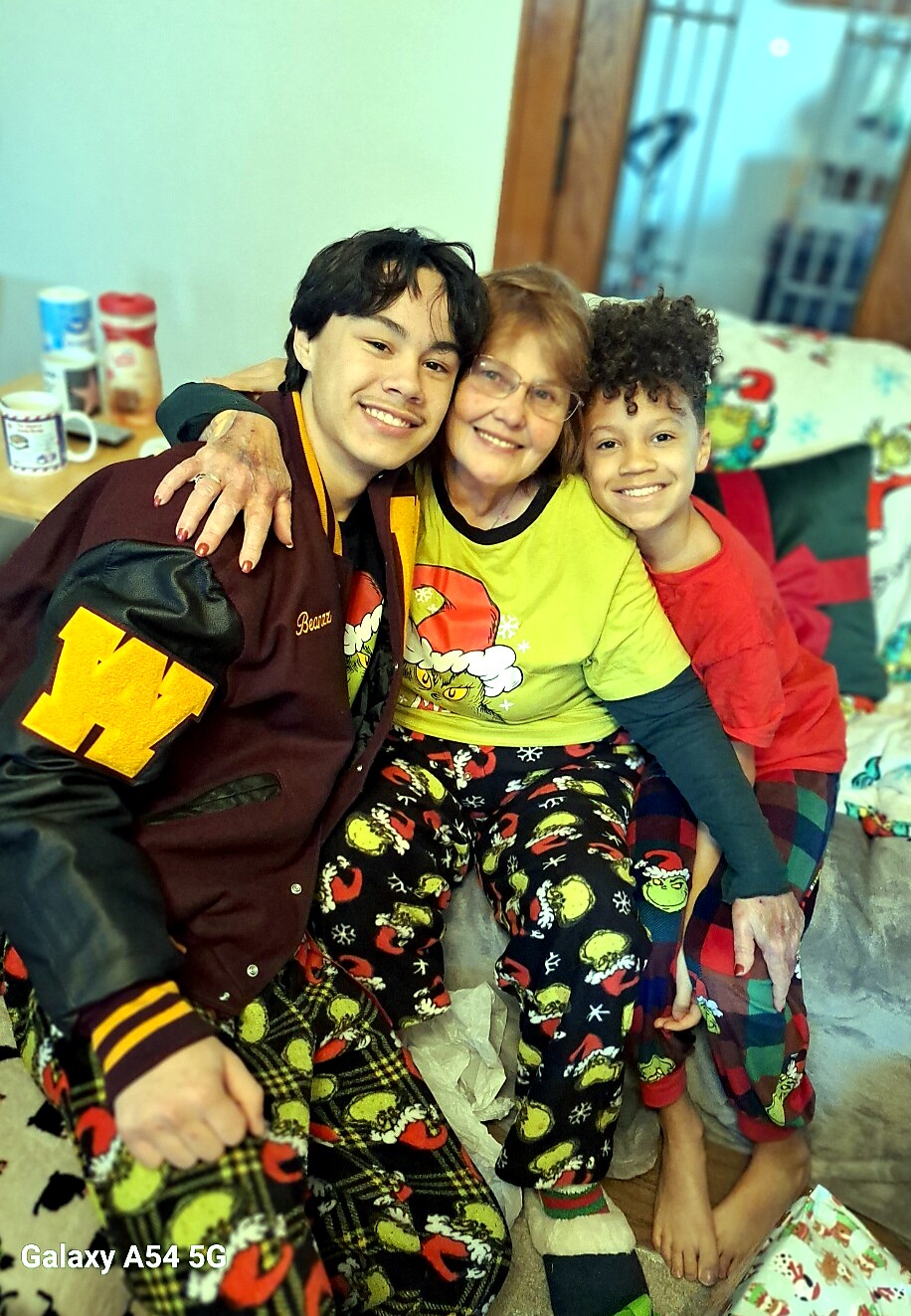 Three generations posing together on a couch in festive pajamas, smiling warmly at the camera.