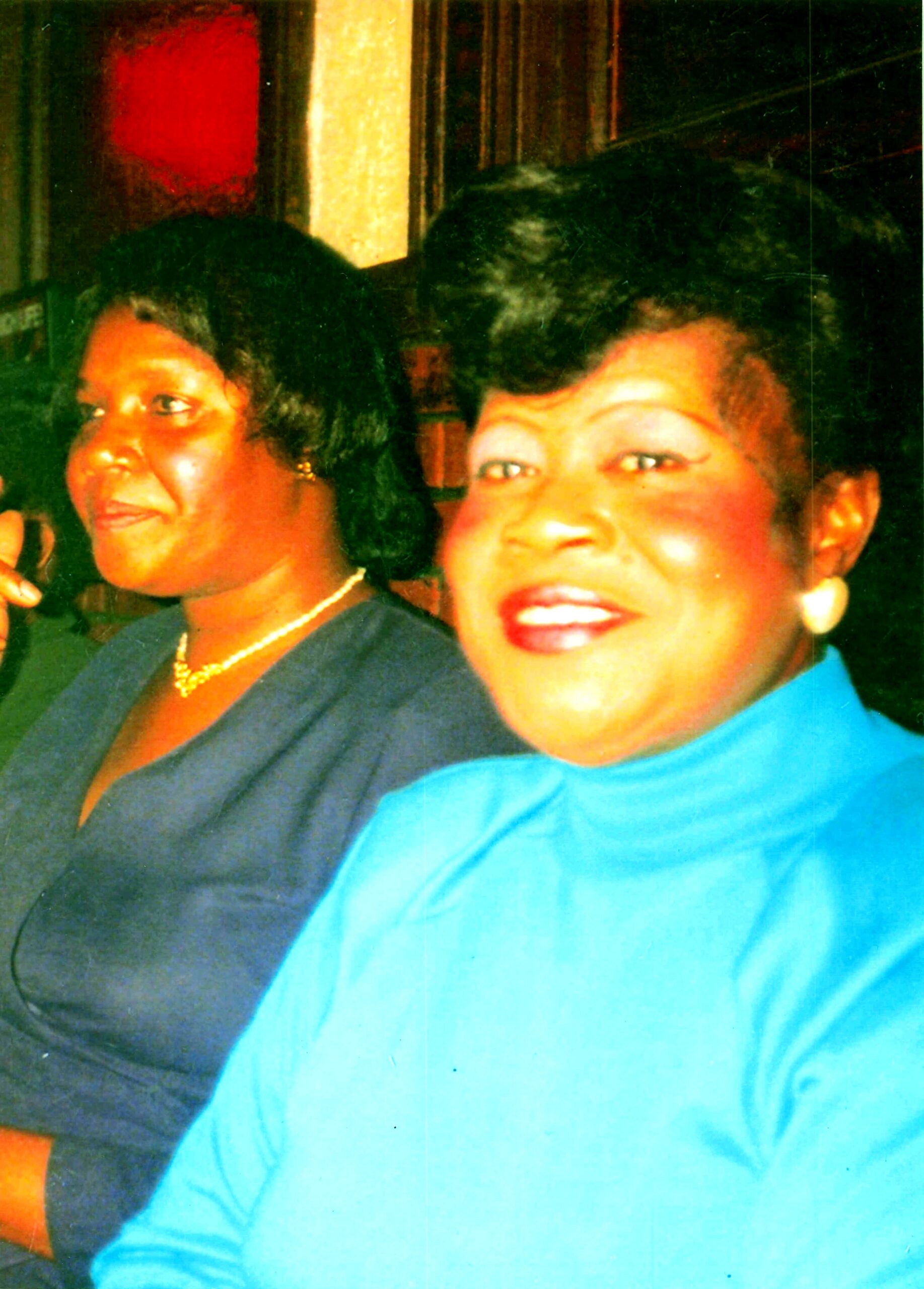 Two women pose for a photo at a social event, smiling toward the camera in a dim room.