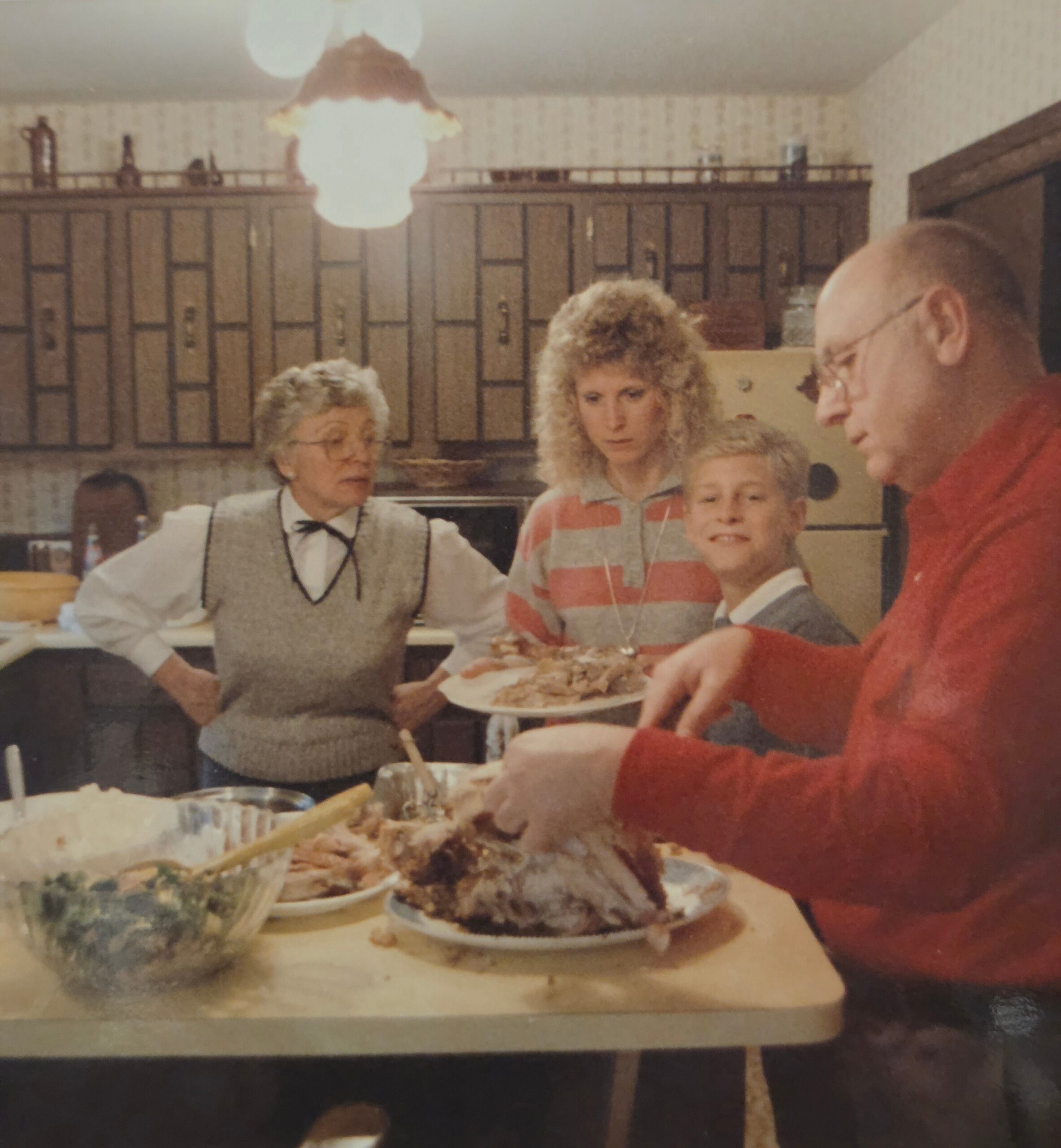 Family gathered around a dinner table in a kitchen, with a large roasted turkey and side dishes as they share a meal.