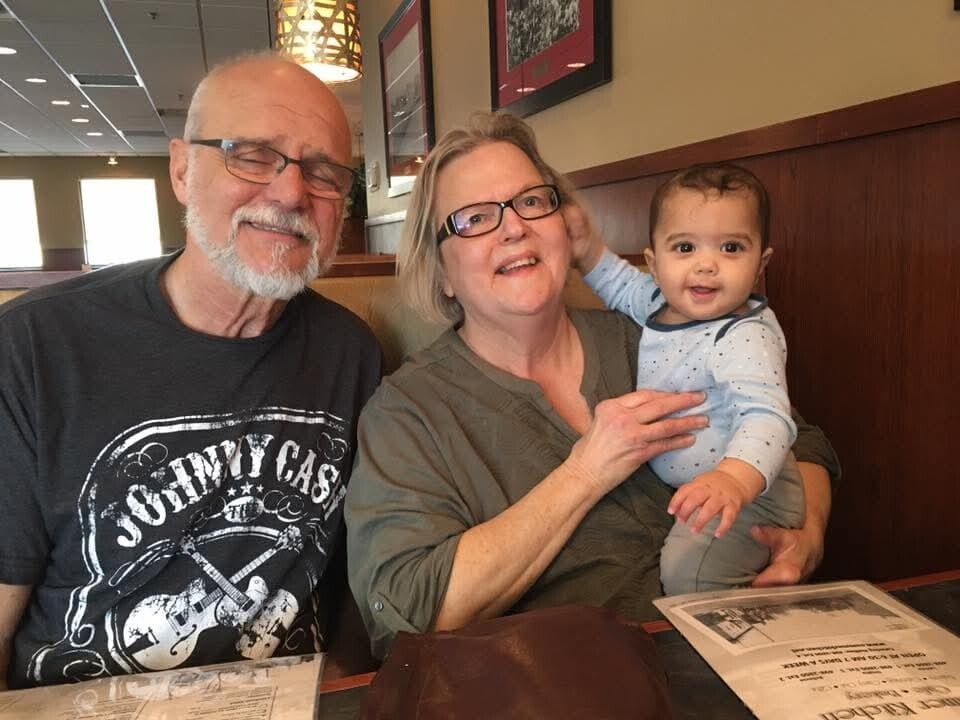 Grandfather, mother, and baby smiling together at a restaurant booth.