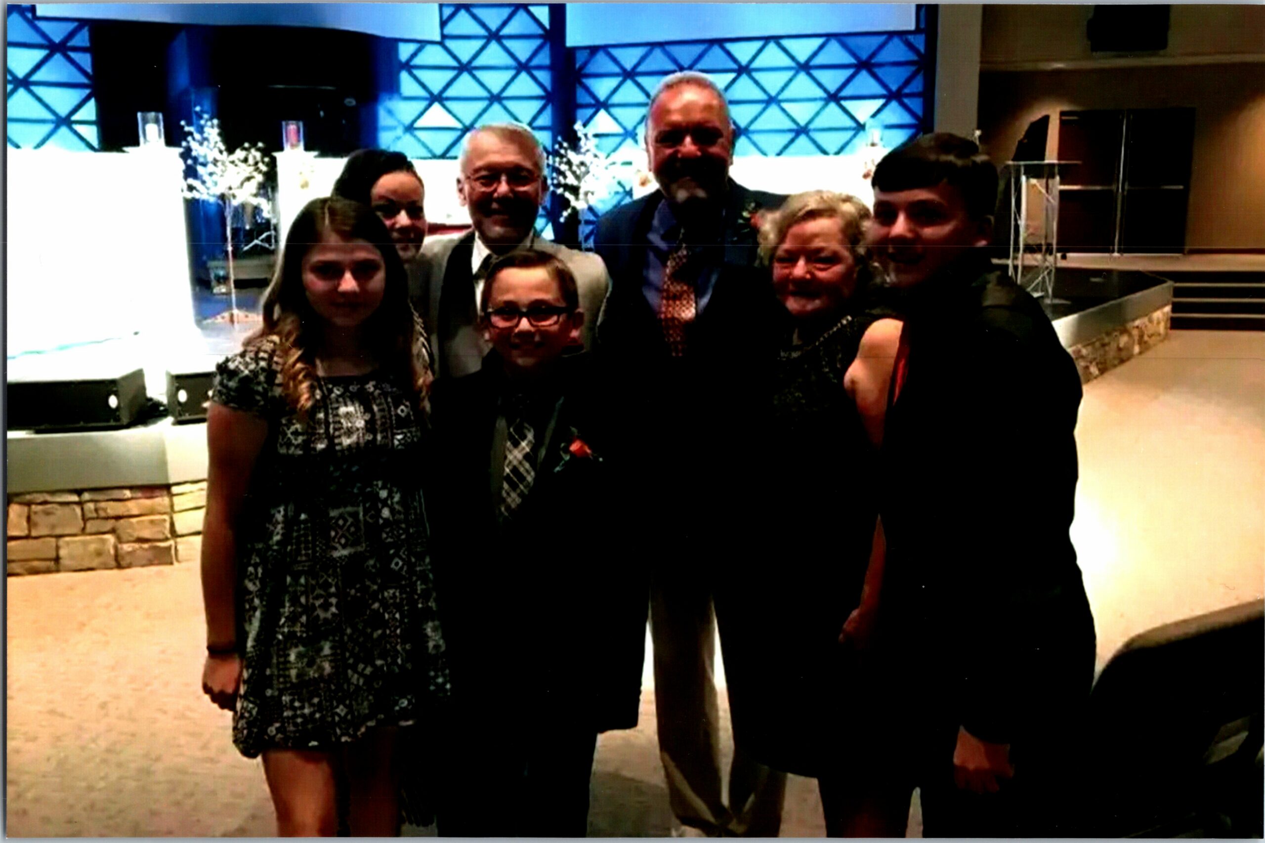 Six adults smiling for a group photo at a formal indoor event, with a blue geometric backdrop.