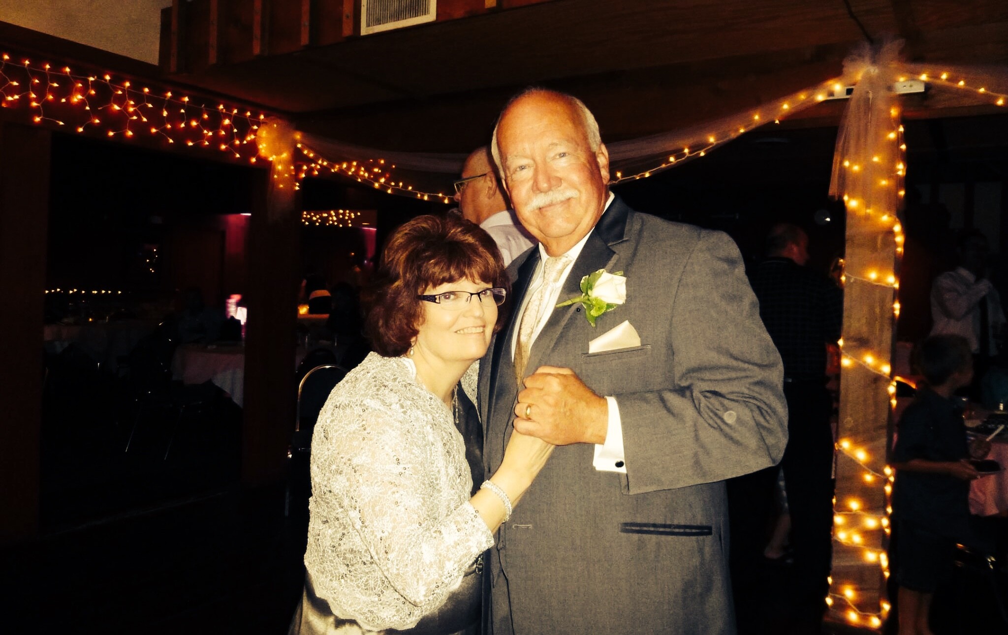 Older couple dancing at a party under warm string lights