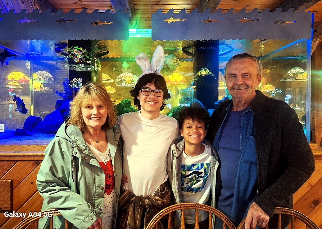 Four people smile for a photo in front of a colorful aquarium display, one wearing bunny ears headband.