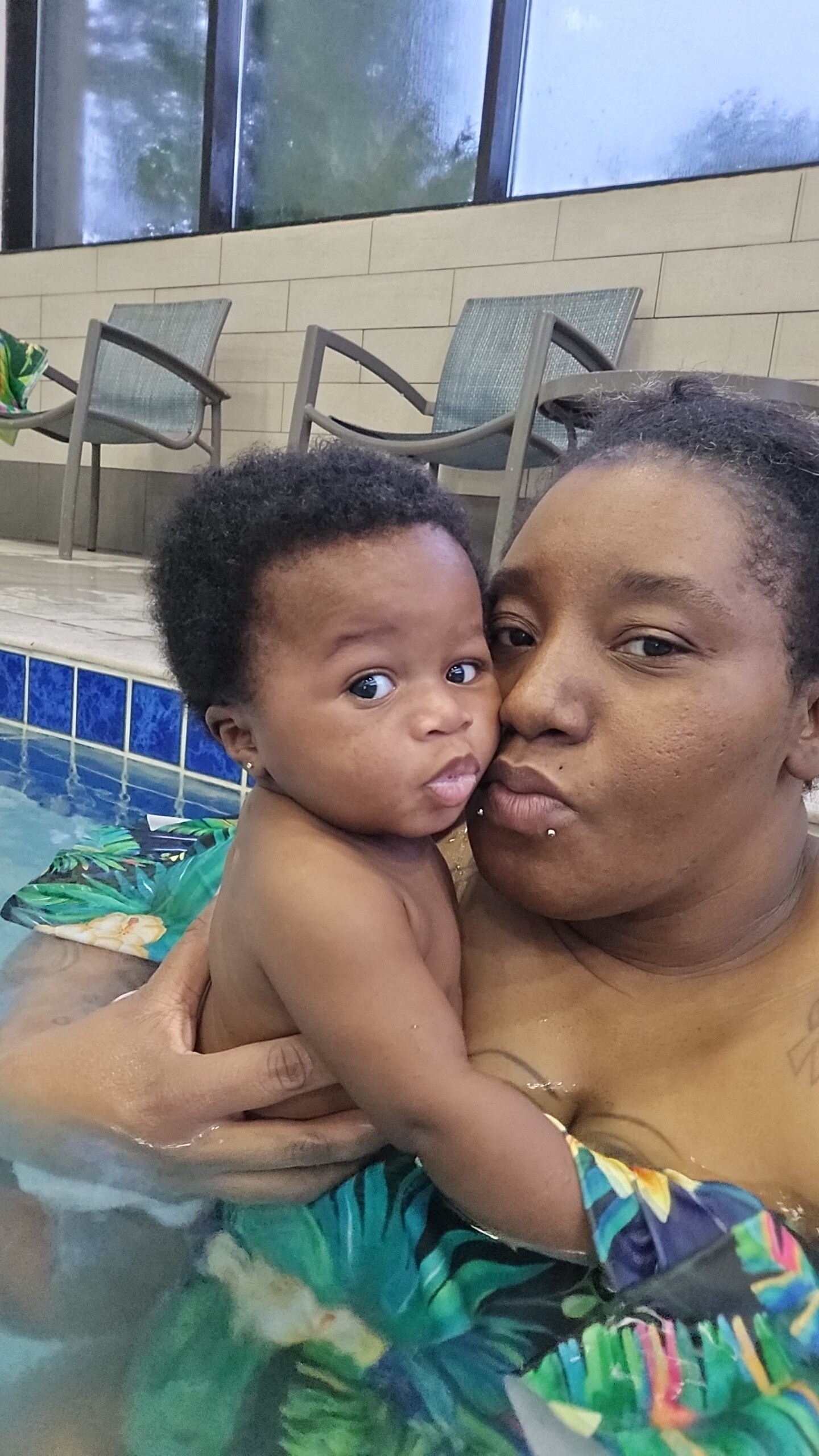Close-up of a woman holding a baby in a swimming pool, both looking at the camera.