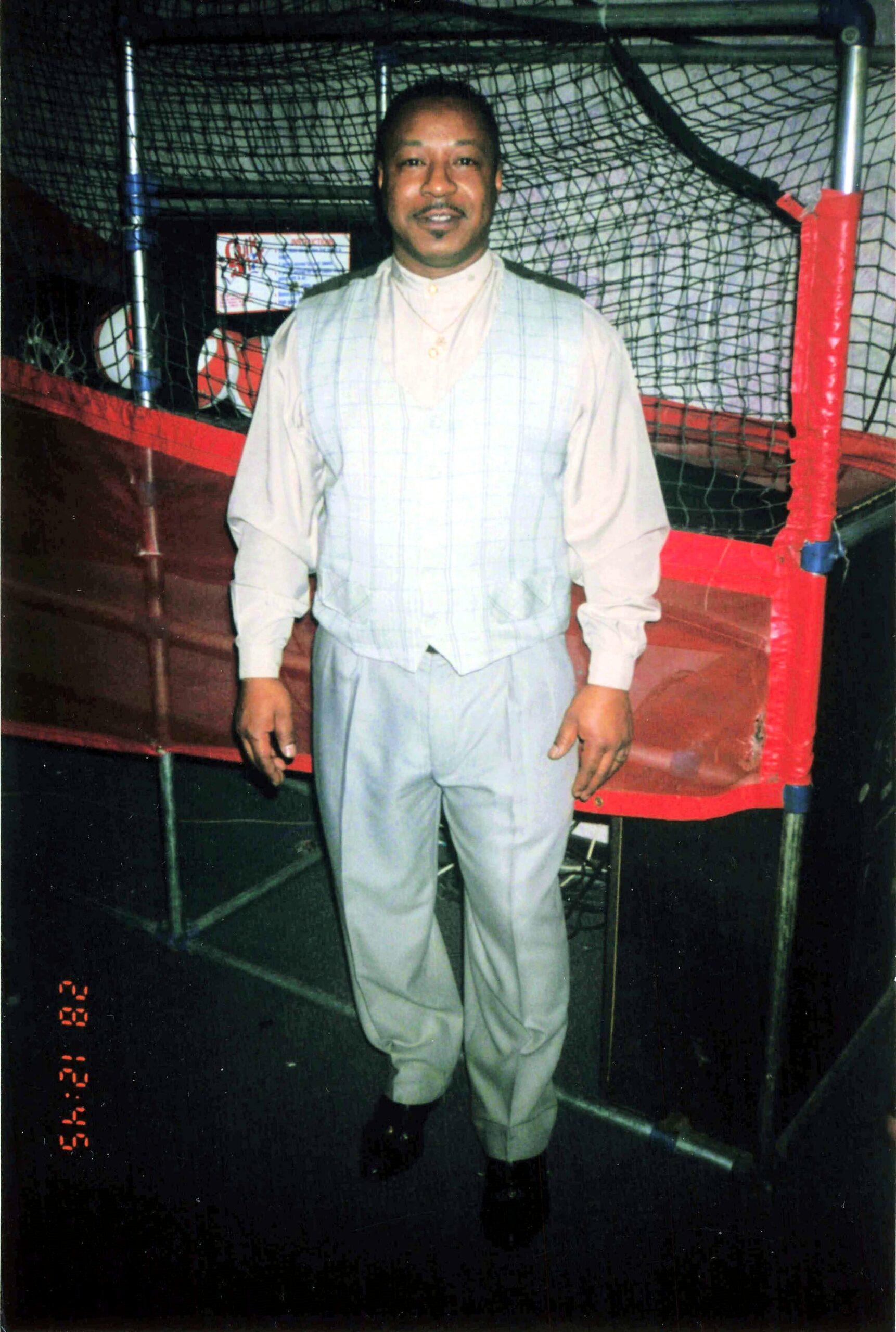 Man in a light outfit standing in front of a boxing ring, smiling at the camera.