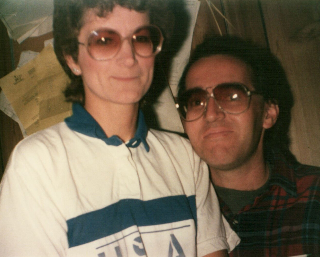 Two people posing closely for a photo: a woman with short hair and large sunglasses on the left, a man with tinted glasses on the right.