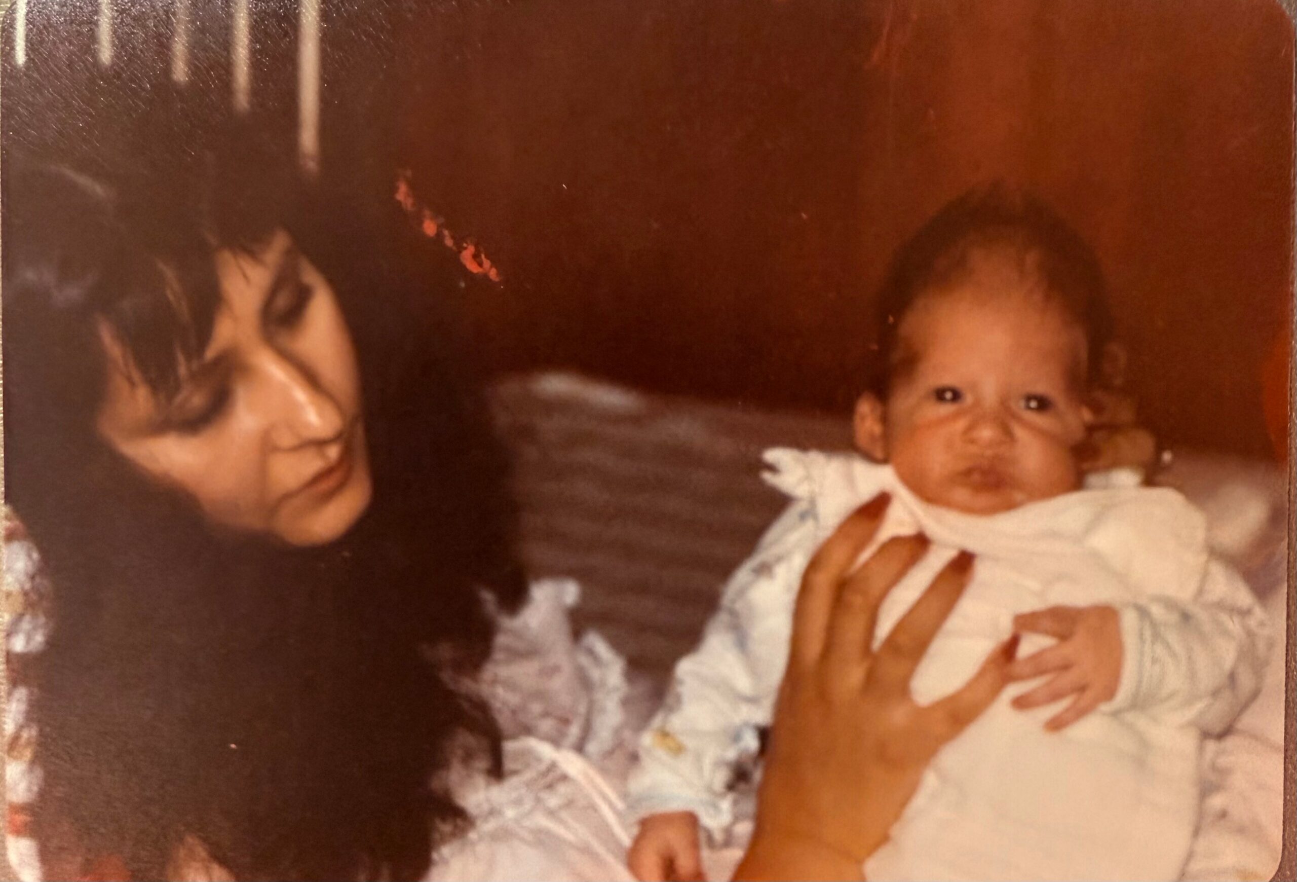 Mother cradling a smiling baby in a light-colored outfit, indoors.
