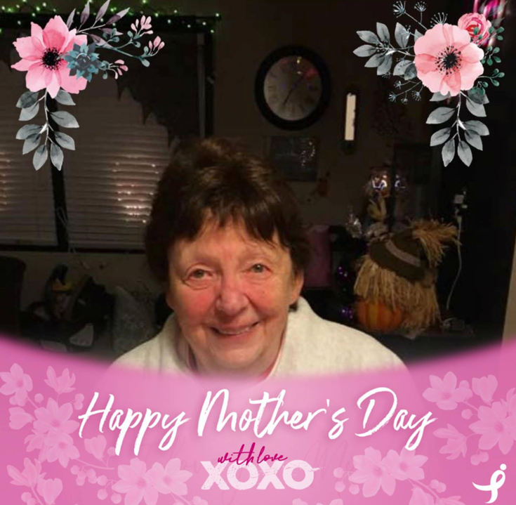 Smiling elderly woman indoors, with a pink ‘Happy Mother's Day’ banner and floral corner decorations framing the photo.