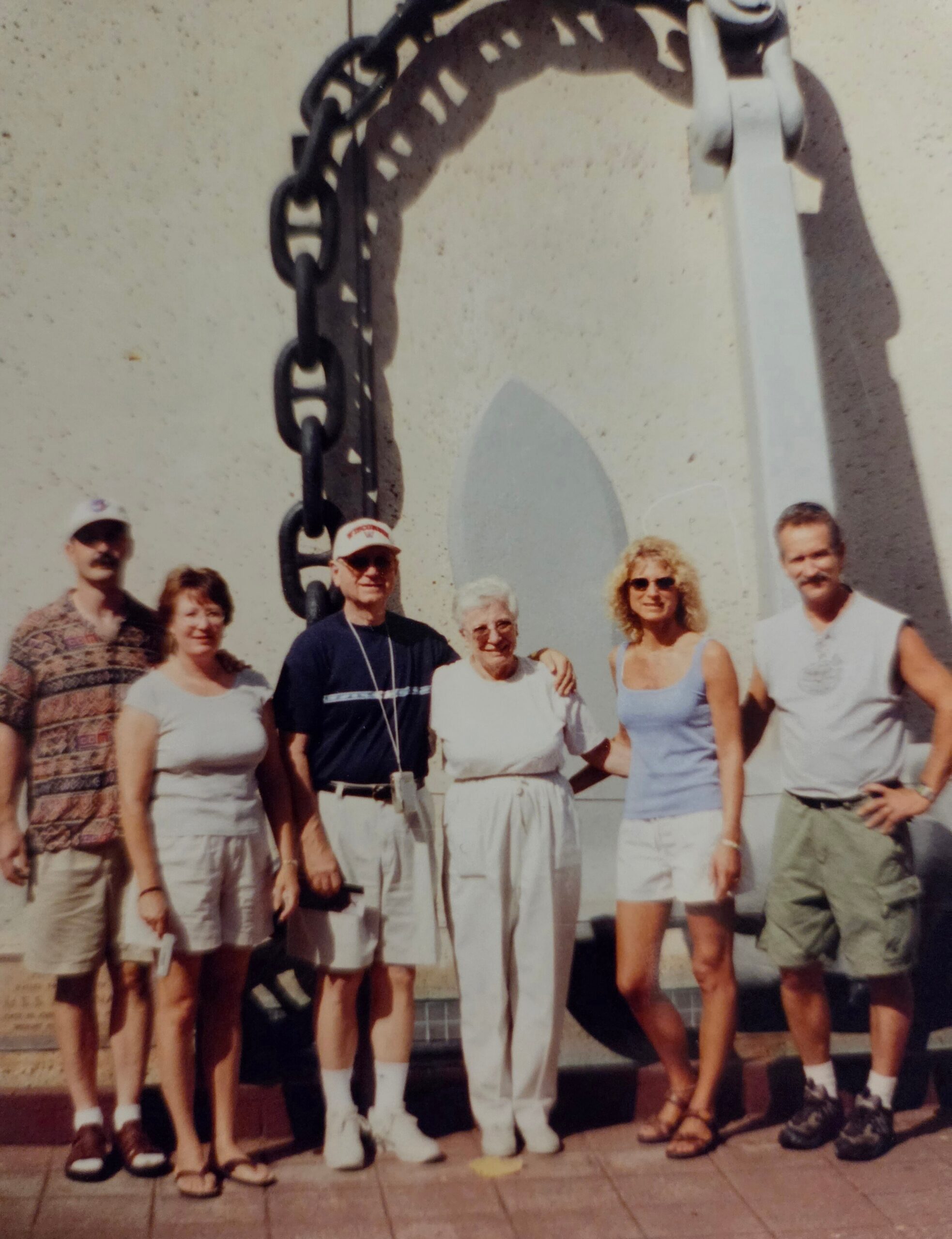 A group of adults posing for a photo outdoors in front of a large decorative metal chain and a surfboard sculpture.