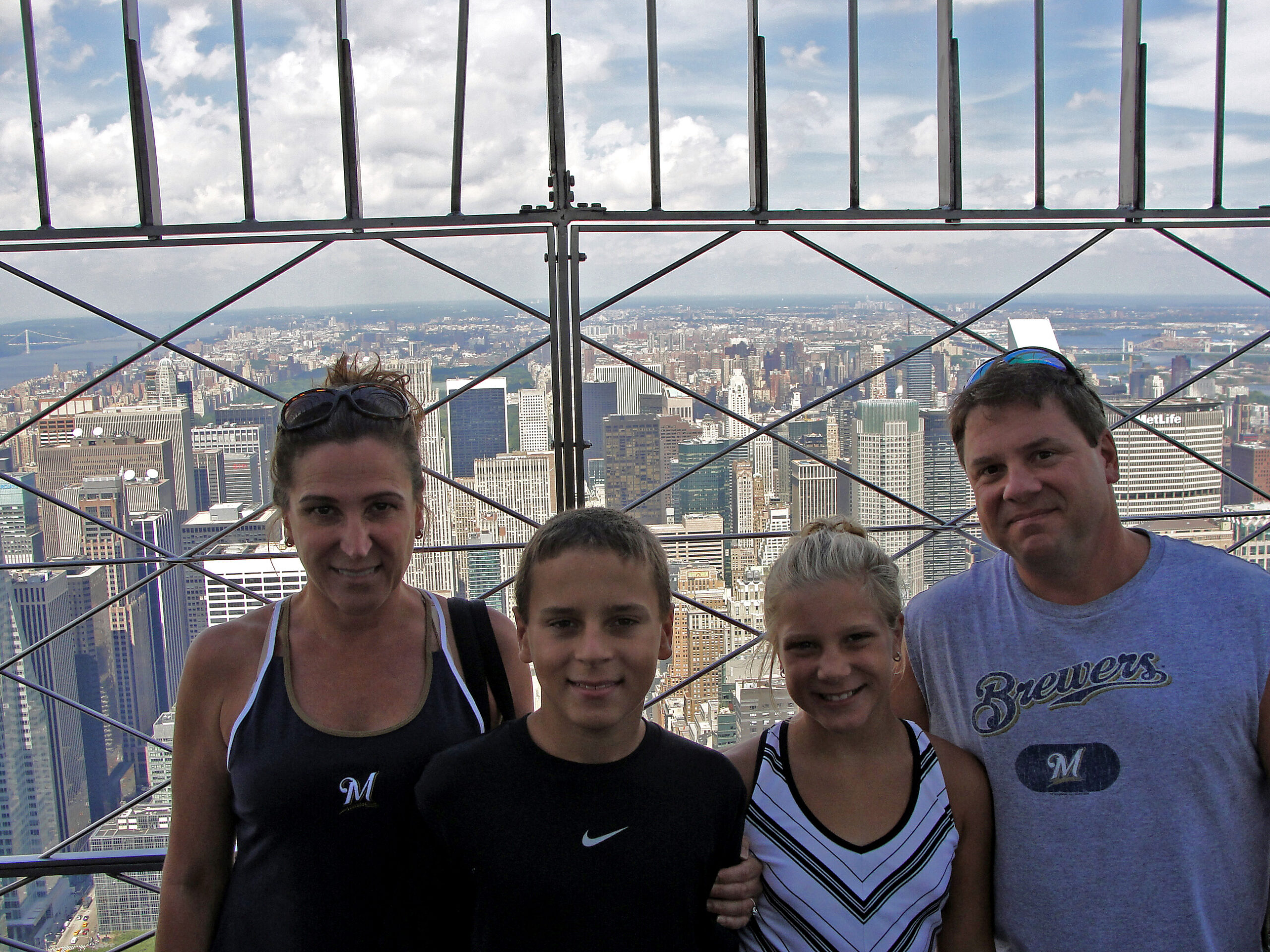 Five people pose for a photo on a high-rise observation deck with a city skyline and river in the distance behind them.