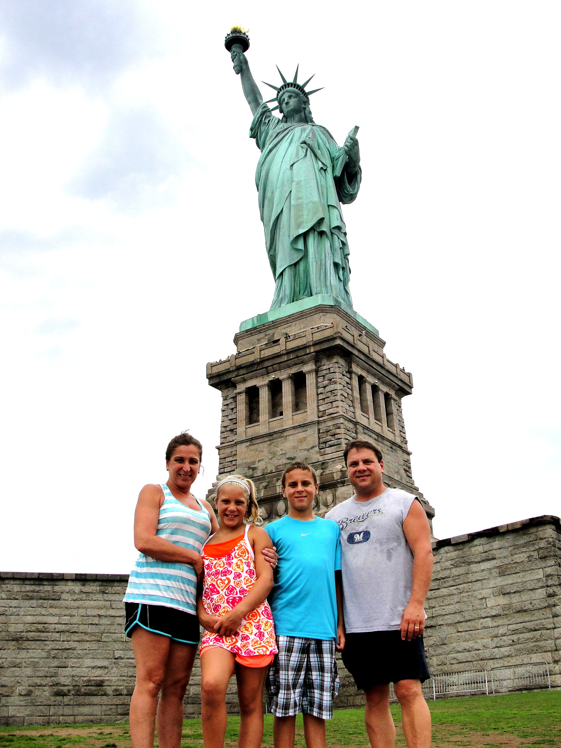 Family posing in front of a replica Statue of Liberty on a stone pedestal.