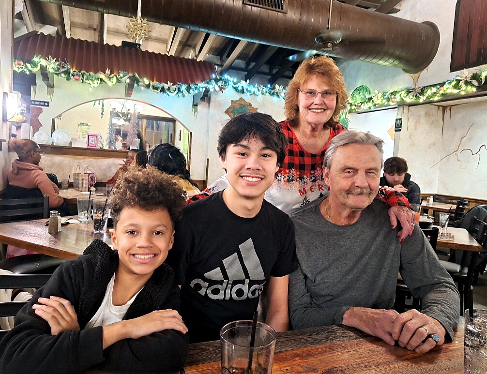 Family of four posing at a restaurant table, with Christmas garlands and string lights overhead.