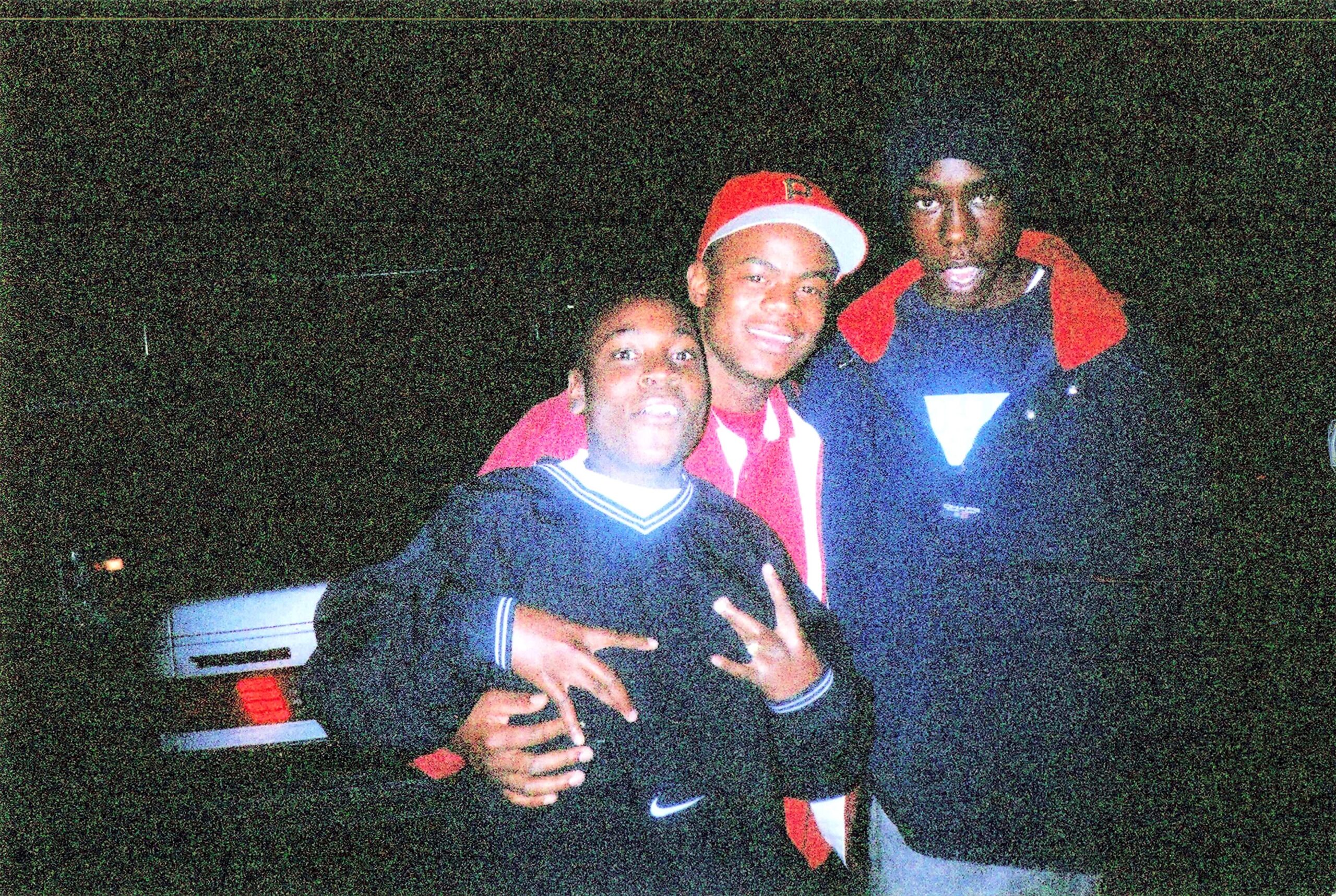Three young men pose closely for a nighttime group photo, smiling at the camera and making peace signs.