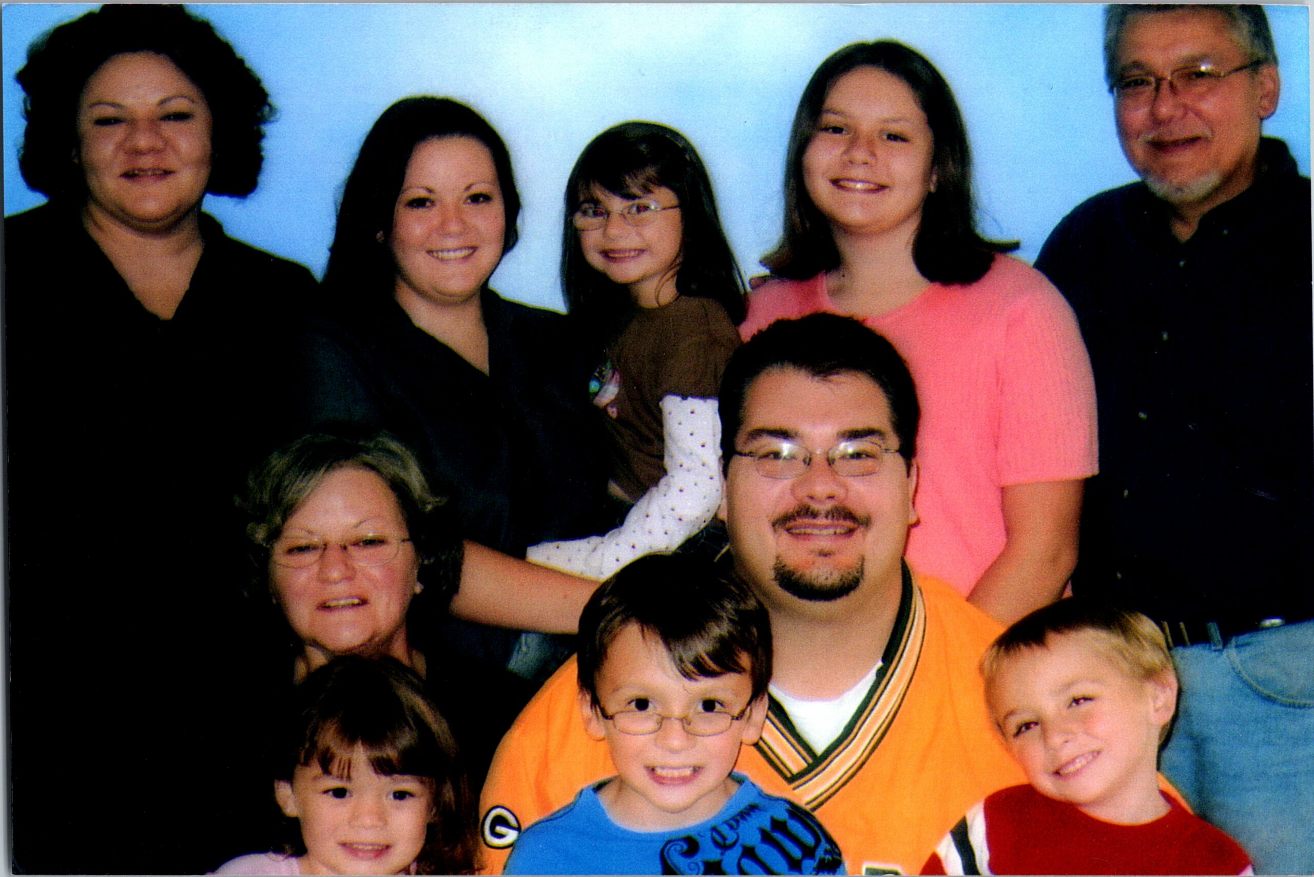 Group photo of smiling adults and children posing together in front of a blue background; everyone looks at the camera.