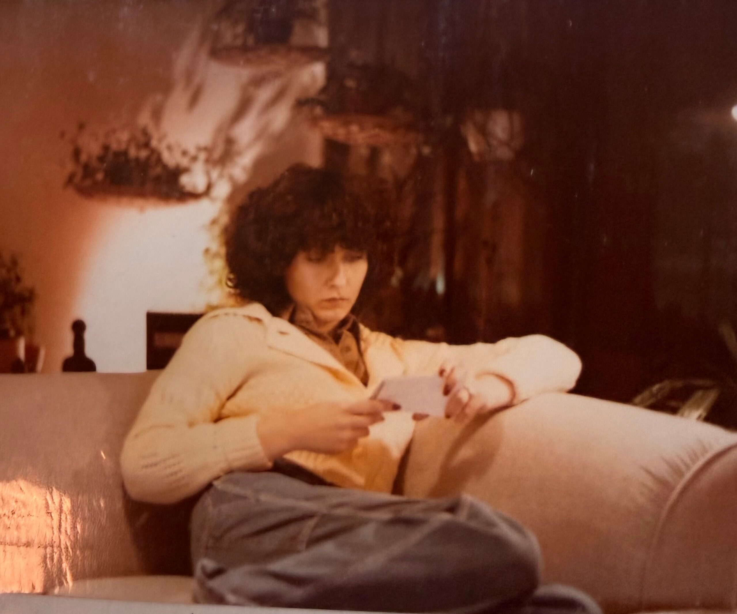Child with curly hair sits at a table, drawing on a sheet of paper in a warm, cozy room.