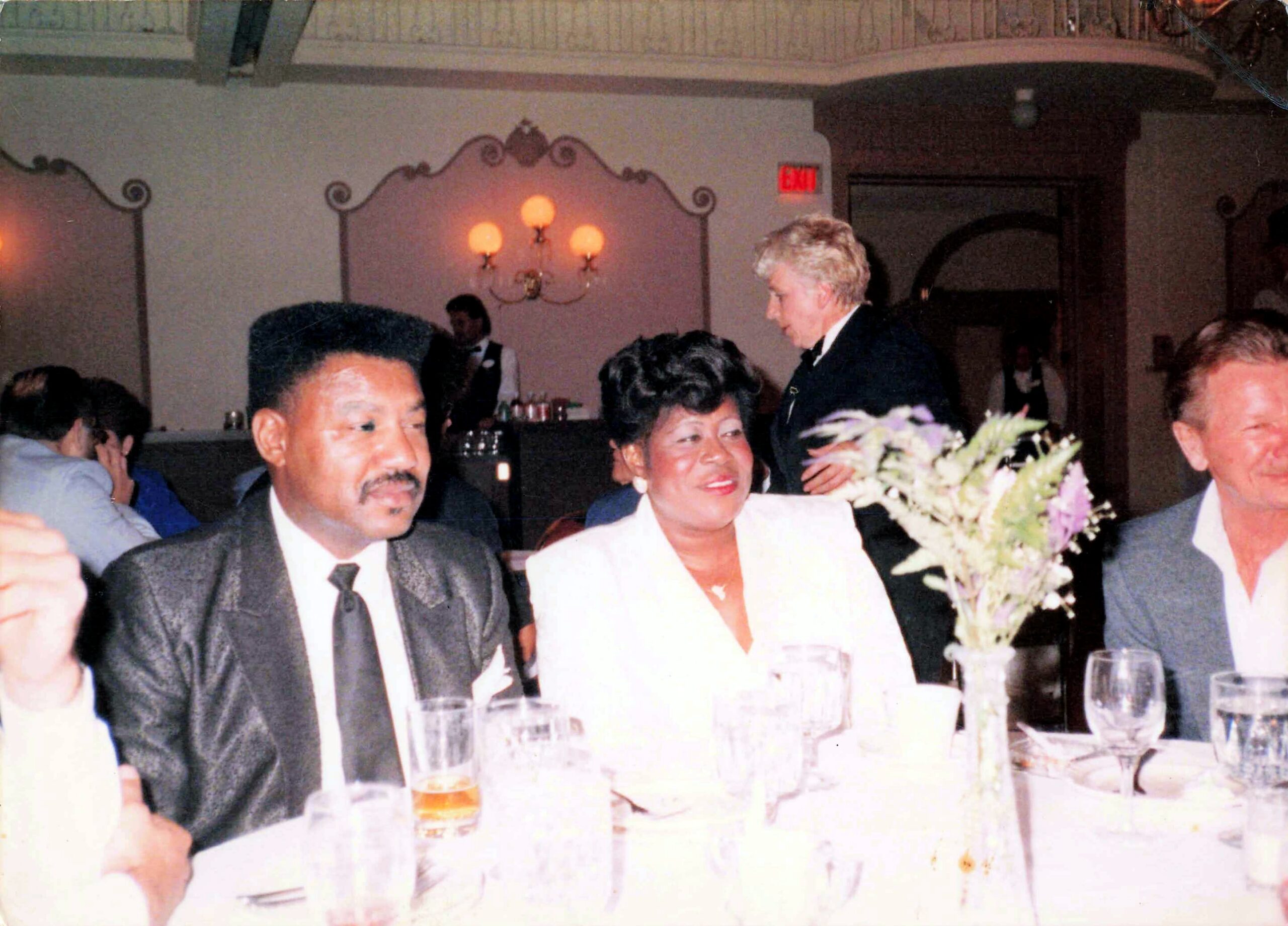 Guests seated at a banquet table in a formal dining hall with drinks and a bouquet centerpiece.