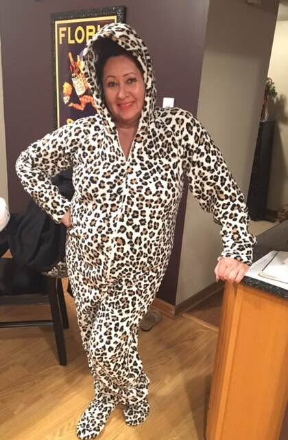 Woman in a leopard-print onesie with hood up, standing with one hand on her hip in an indoor setting.