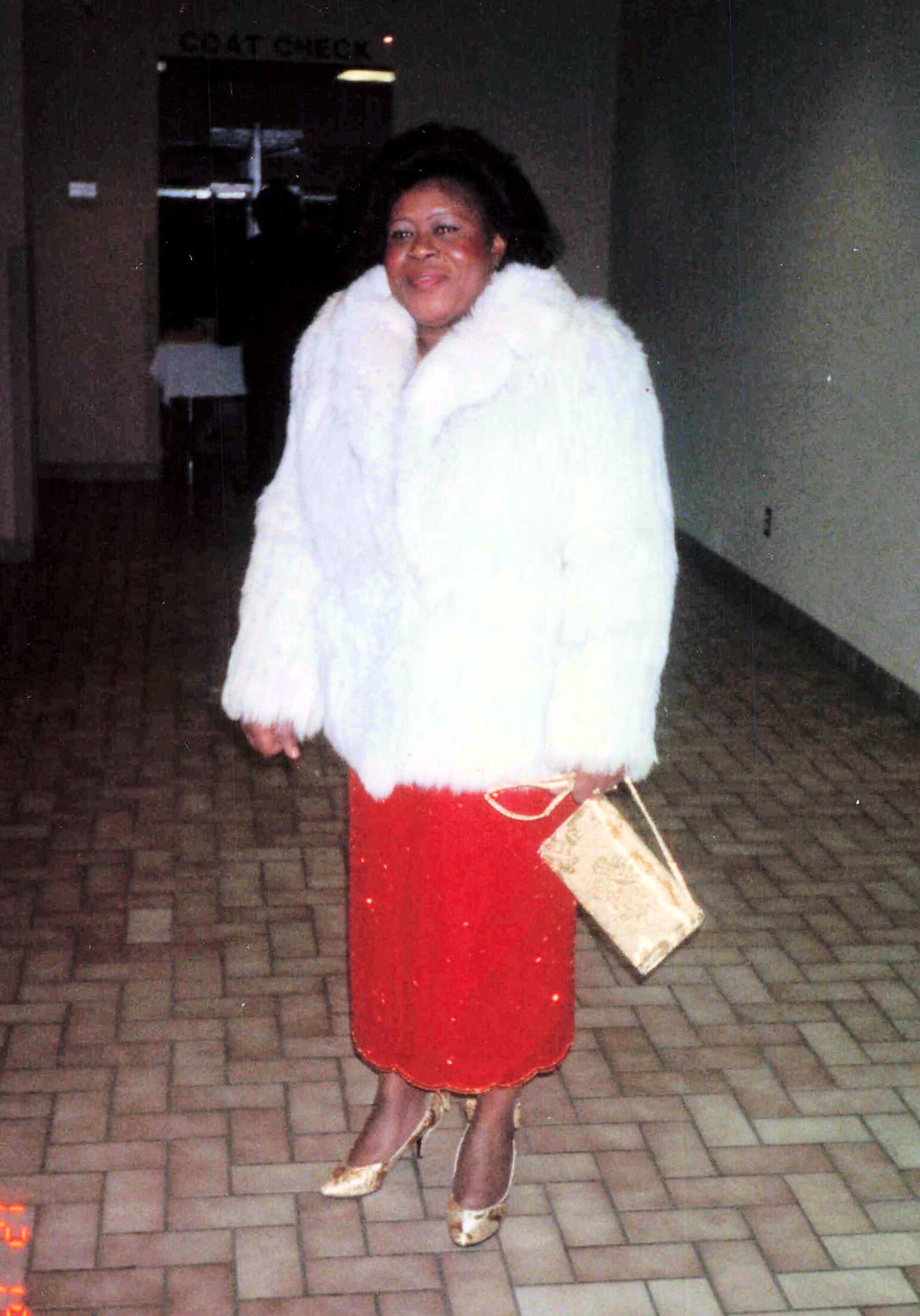 woman in a white fur coat, red sequined skirt, gold heels, and a gold clutch standing on a brick-paved floor