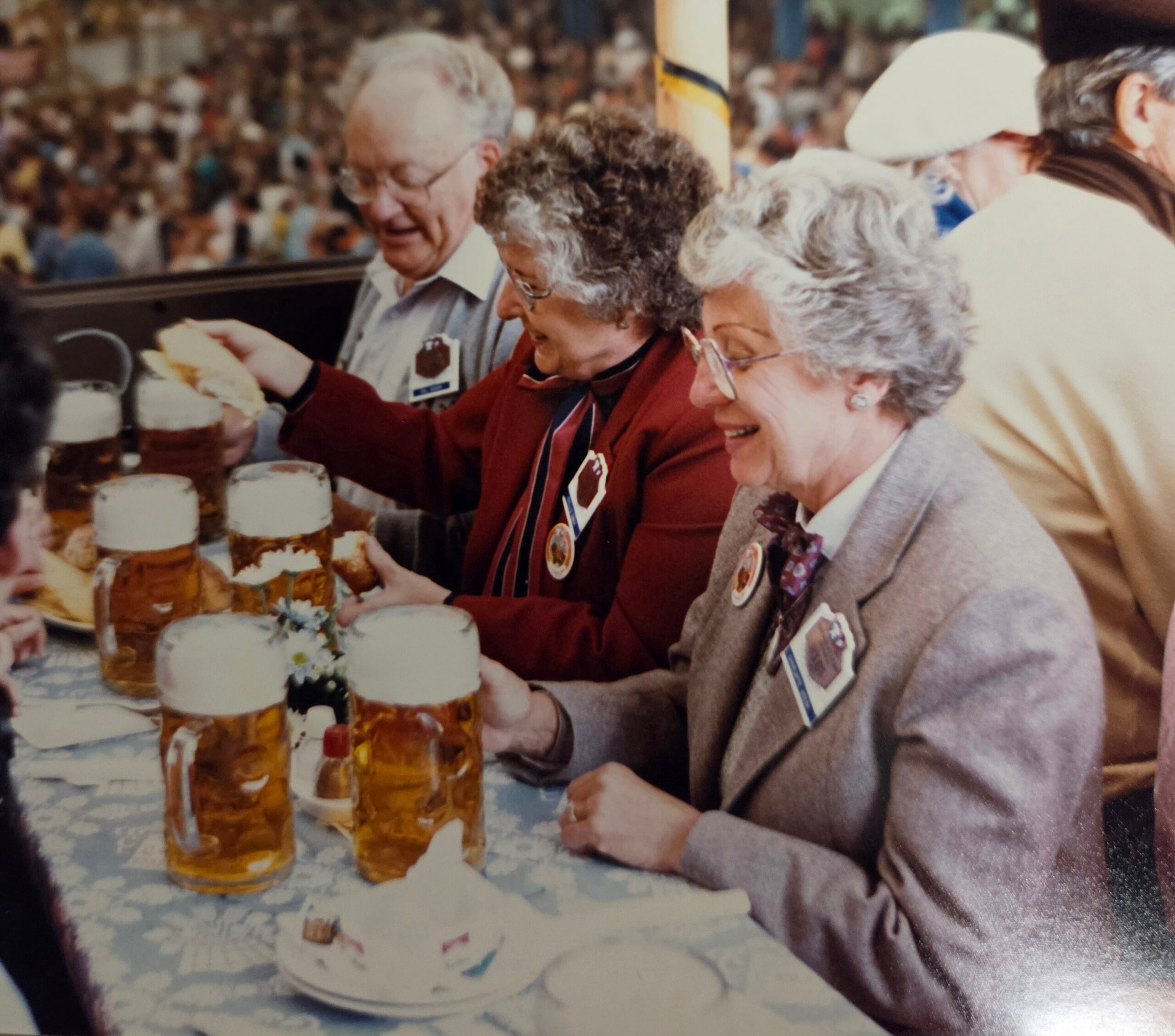 Senior group at a celebration gathered around a table with small cakes and jars, smiling and chatting.