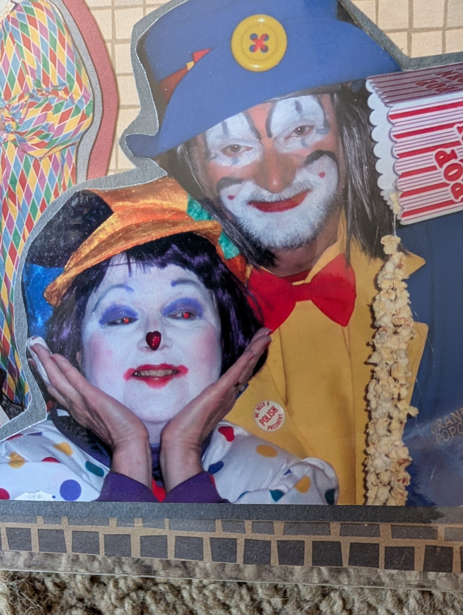 Two people dressed as clowns with white face makeup and red noses, posing in a colorful scene.