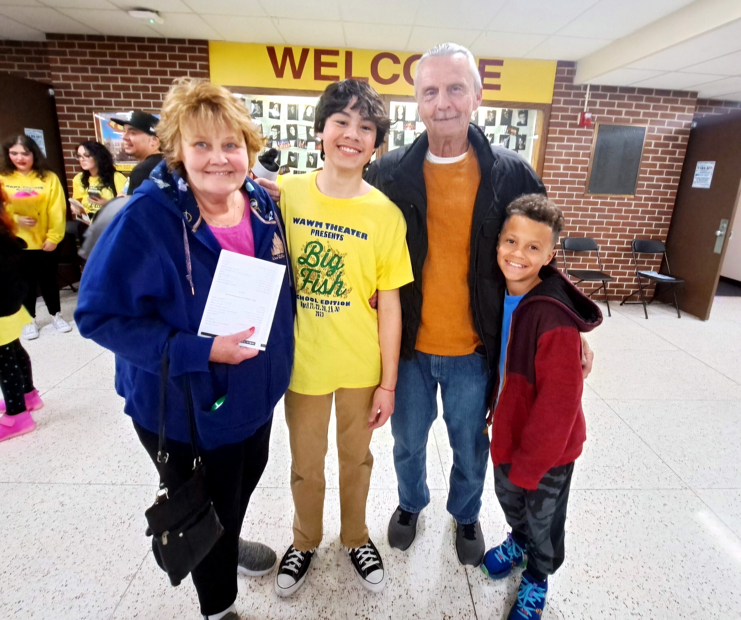 Group of five people smiling for a photo in a school hallway with a yellow Welcome sign behind them.