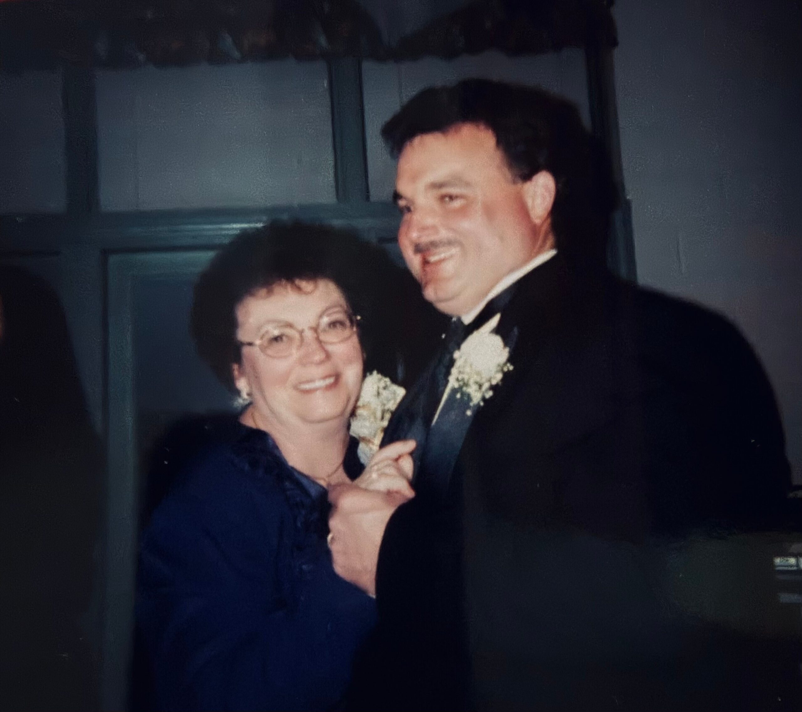 Smiling elderly woman with glasses dancing with a man in a dark suit at a formal event or wedding.