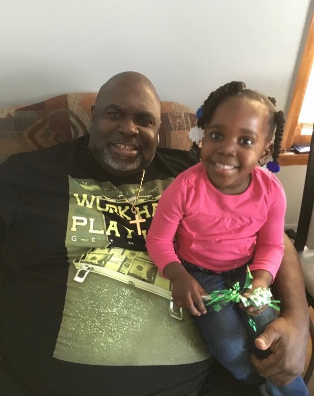 Smiling man with a goatee and a young girl in a pink shirt sitting together on a couch.