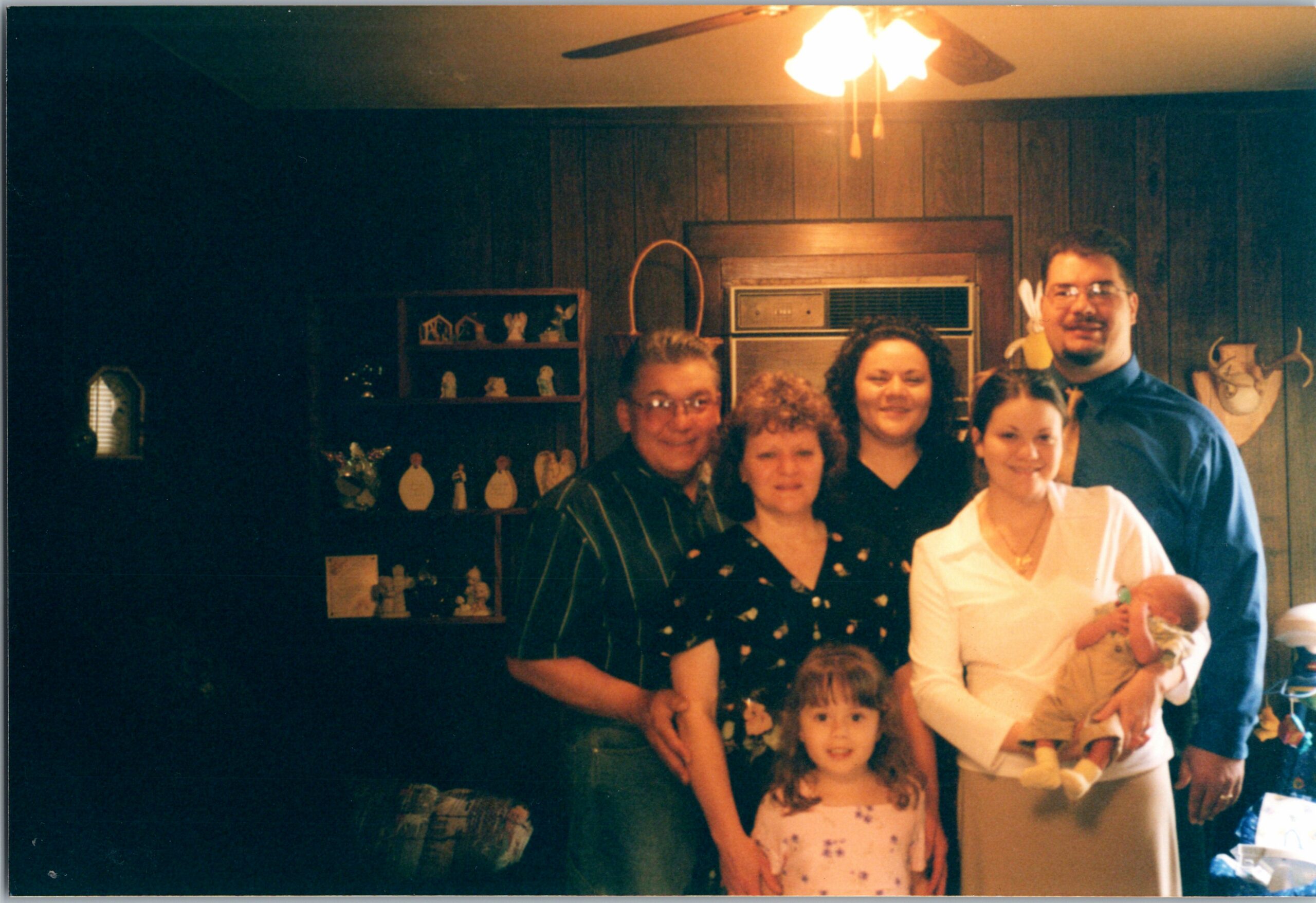 Group family portrait in a living room: adults and children smiling, one baby held by a woman.