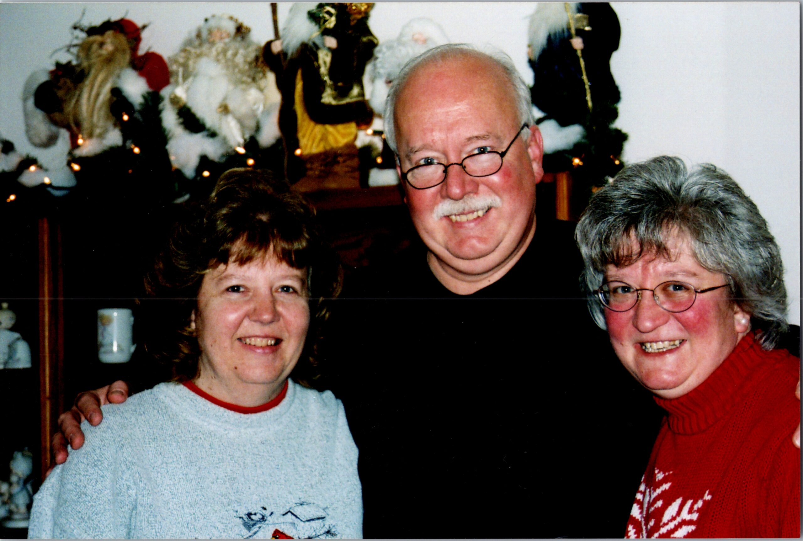 Three adults smile for a Christmas-time group photo indoors, with holiday decorations in the background.