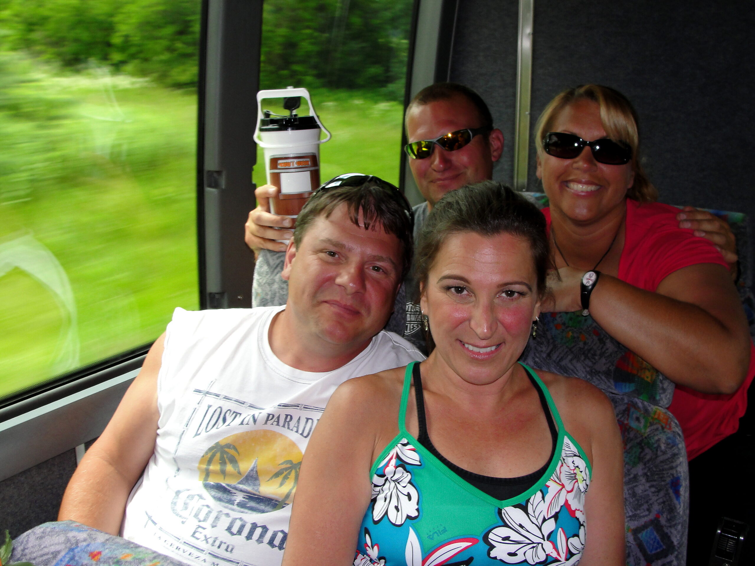 Smiling group of adults posing for a selfie on a bus, all wearing sunglasses and close together.