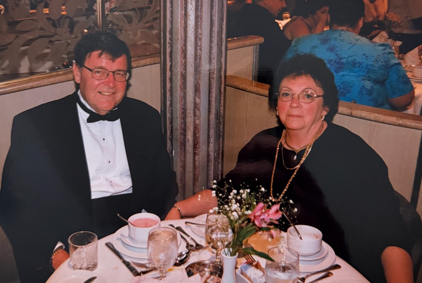 A formally dressed couple seated at a dinner table, smiling at the camera.