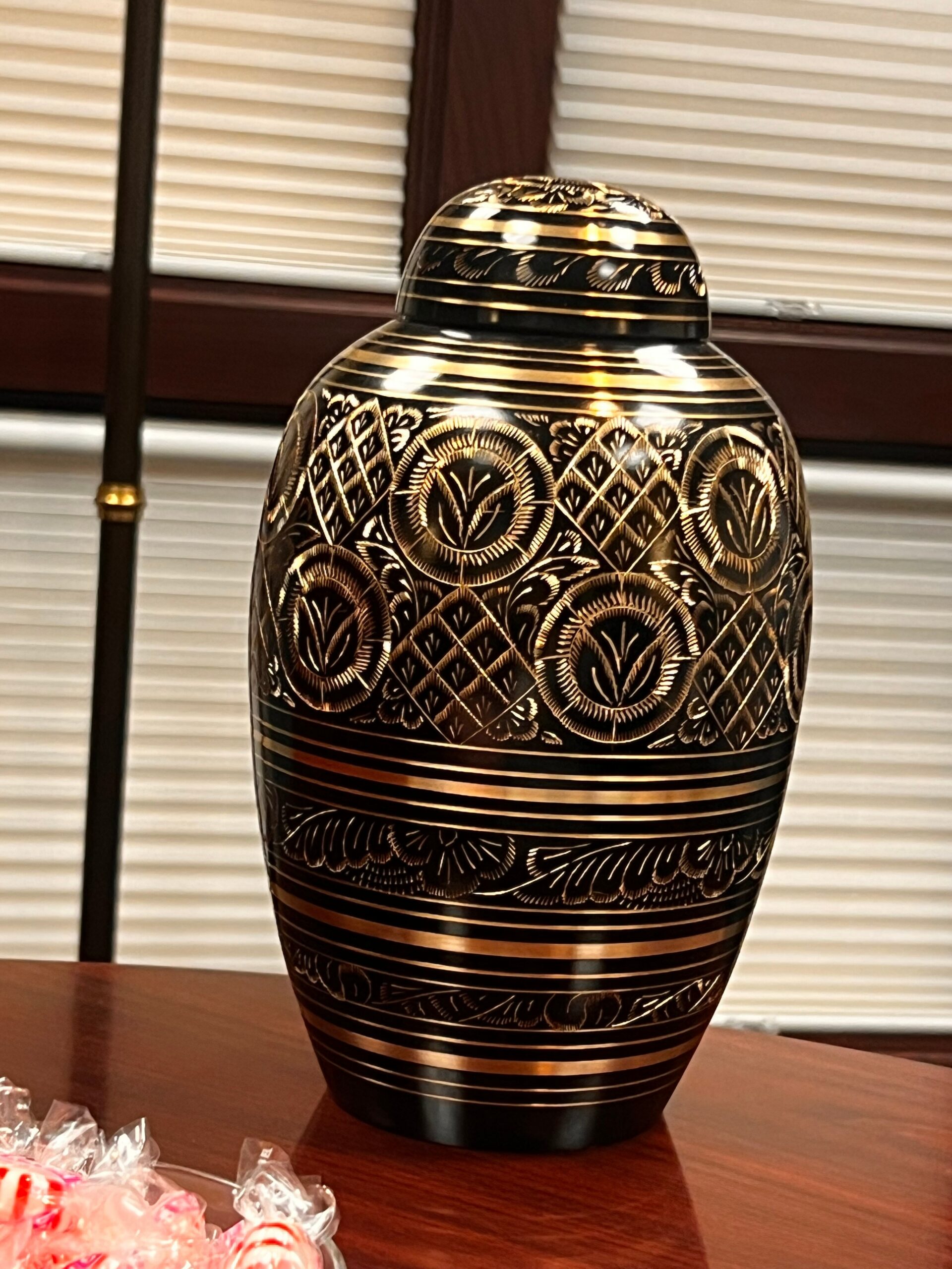 Decorative black ceramic vase with gold geometric and floral patterns on a wooden table.