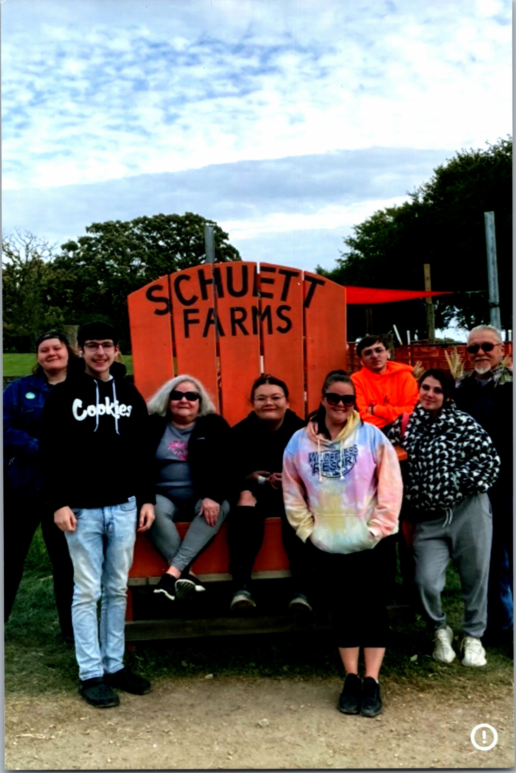Group of people posing in front of an orange Schuett Farms sign outdoors in a park setting.