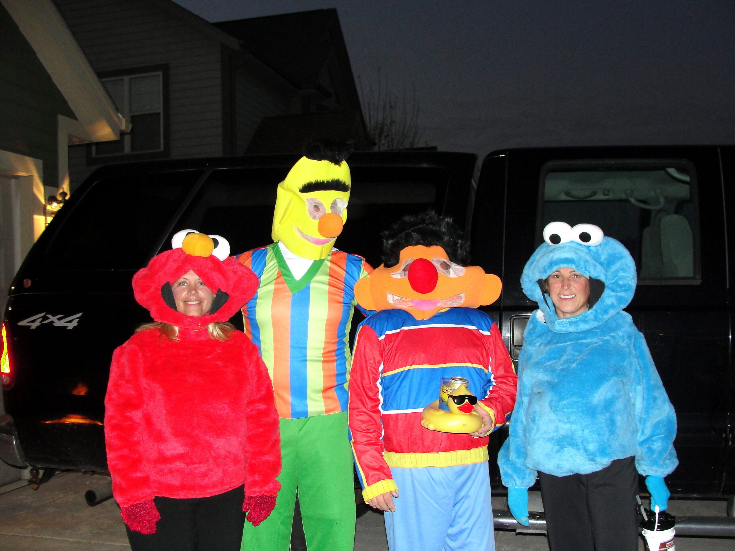 People in Sesame Street costumes posing in front of a black SUV at night.