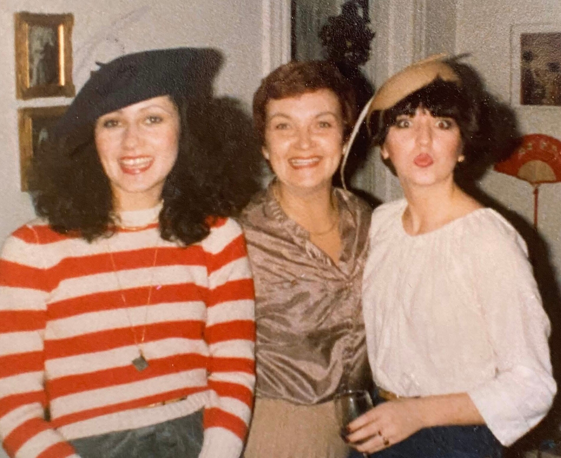 Three women posing indoors for a casual group photo; left in red-and-white striped sweater, middle smiling, right in white top making a kissy face.