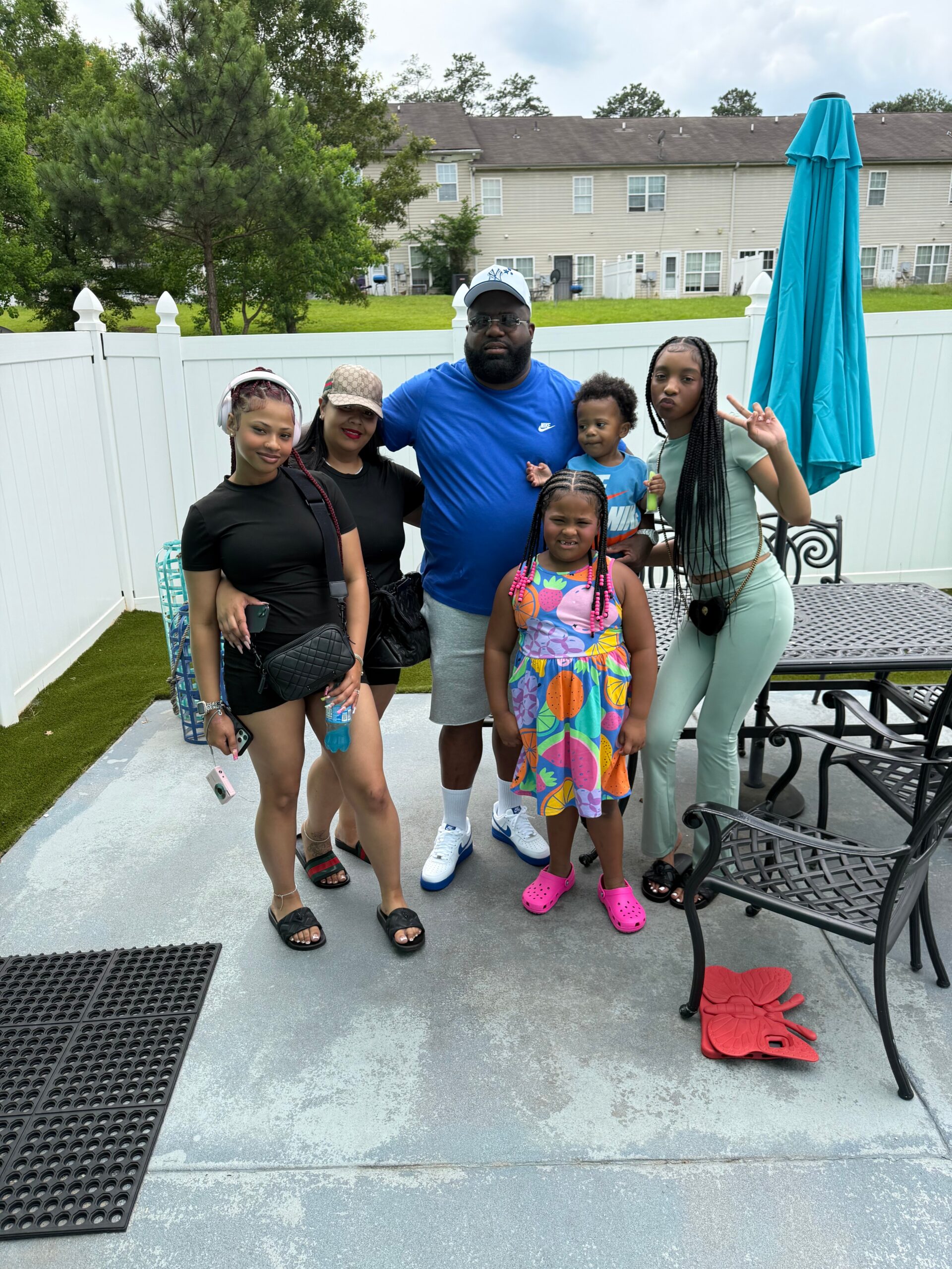 Family posing together on a patio in a fenced backyard, smiling at the camera.