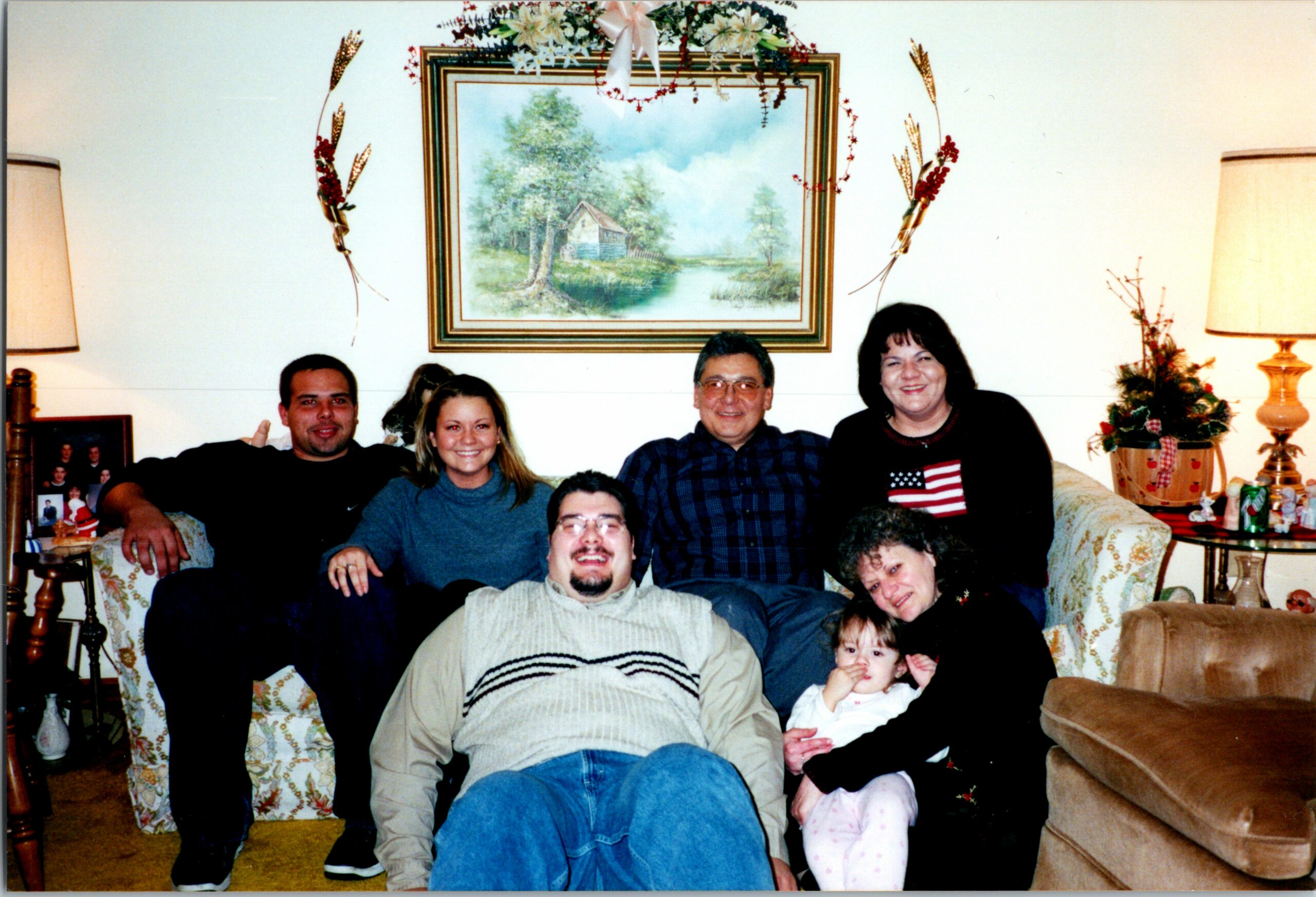 Family group posing on a patterned couch in a living room with holiday decor and a painting behind them