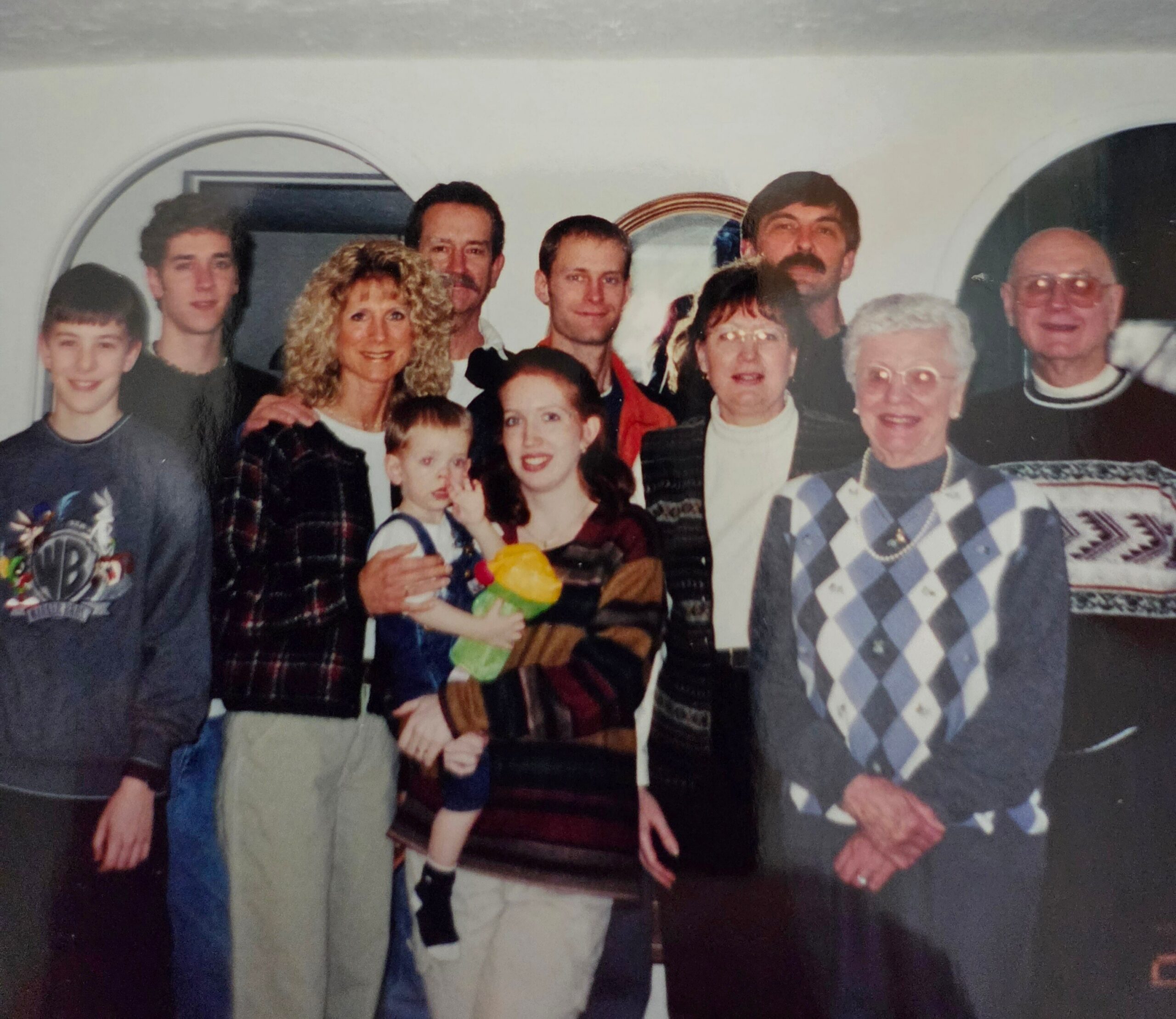 A group of family and friends posing for a photo indoors, smiling at the camera, with children in front and adults behind them.
