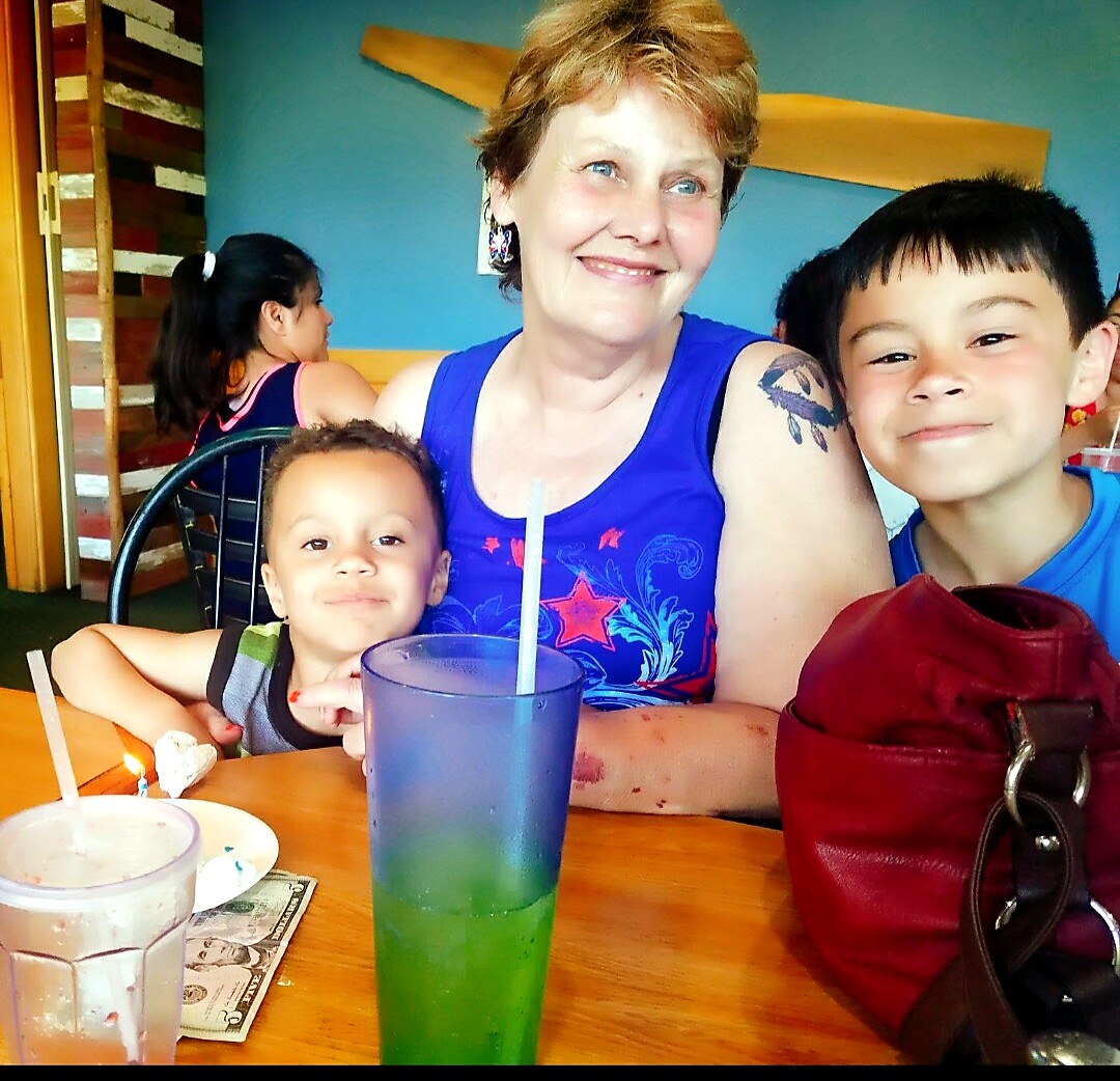 Smiling woman with two children at a wooden table, colorful drinks in front of them in a casual eatery.