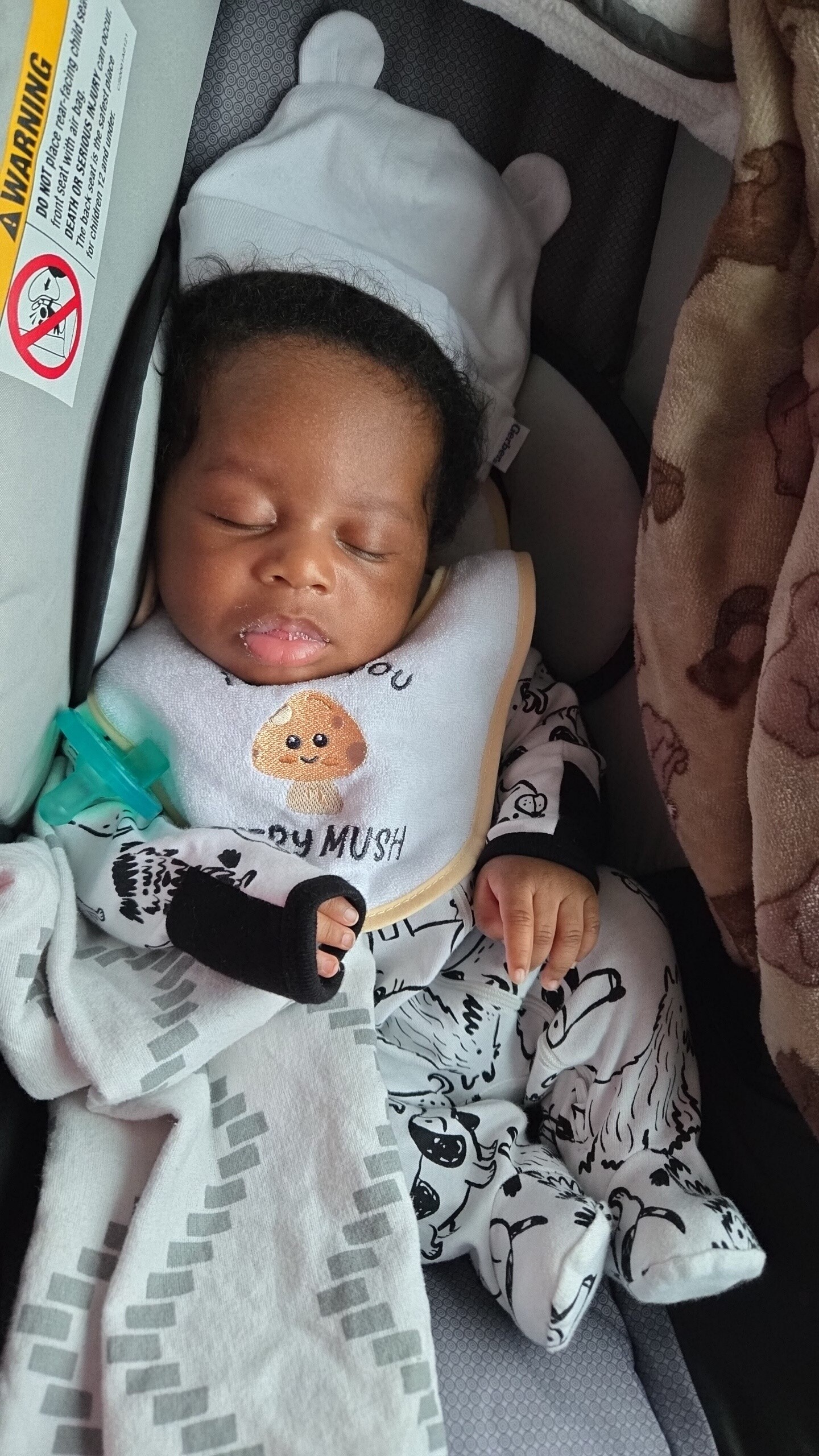 Sleeping infant in a car seat, wearing a light blue bib with a cute mushroom design