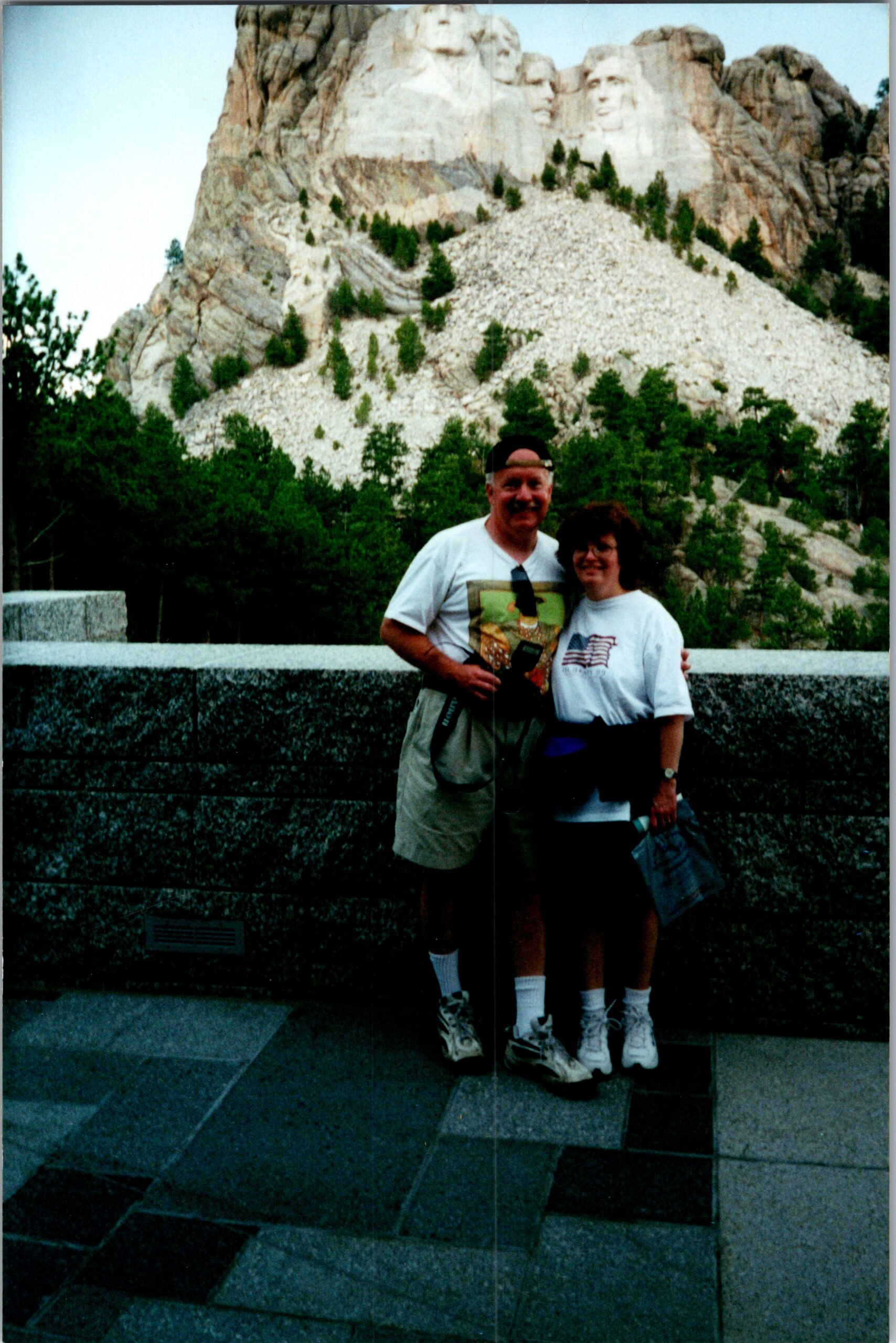 Couple posing and smiling in front of a stone railing with a carved mountain face in the background.