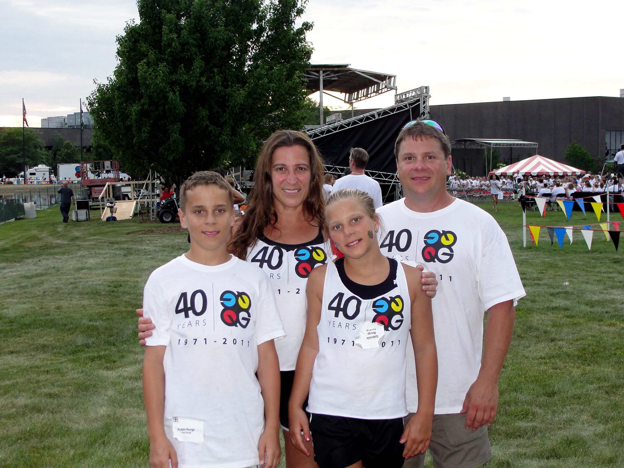 Family of four posing together outdoors at a festival, all wearing white T‑shirts with a 40 years logo.
