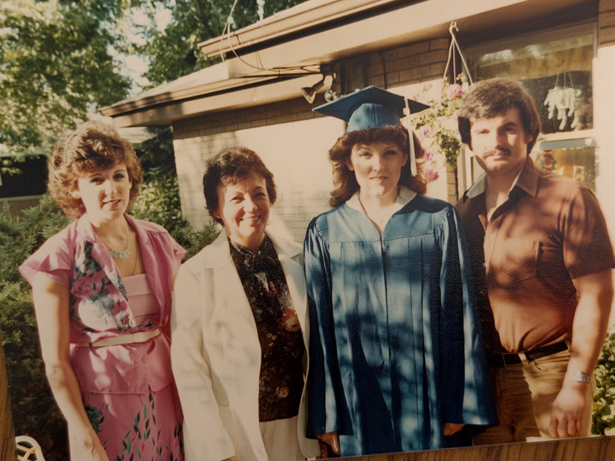Group of four adults posing for a graduation photo; the graduate wears a blue cap and gown.