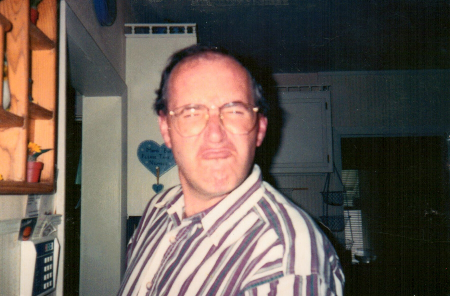Man with large eyeglasses wearing a striped shirt, posing in a late-20th-century storefront or office setting.