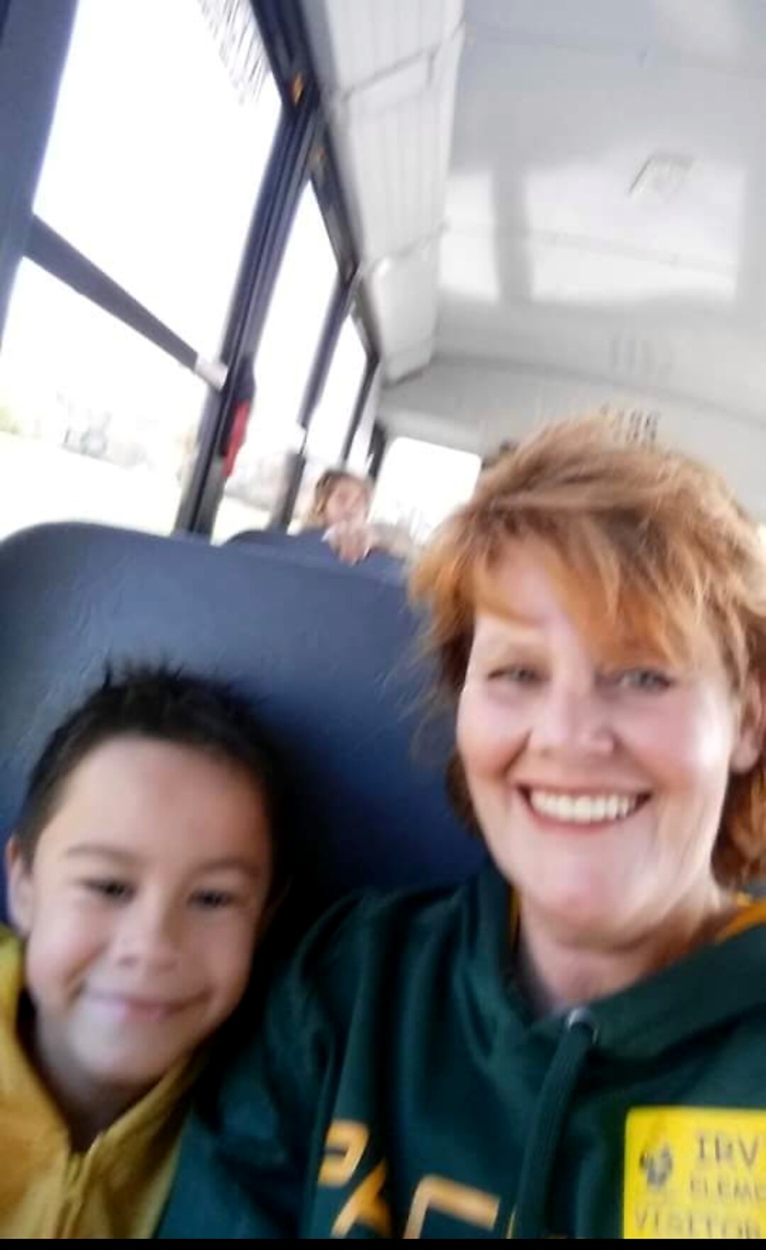 Two people posing for a selfie on a bus: a woman with short red hair and a girl, both smiling at the camera.