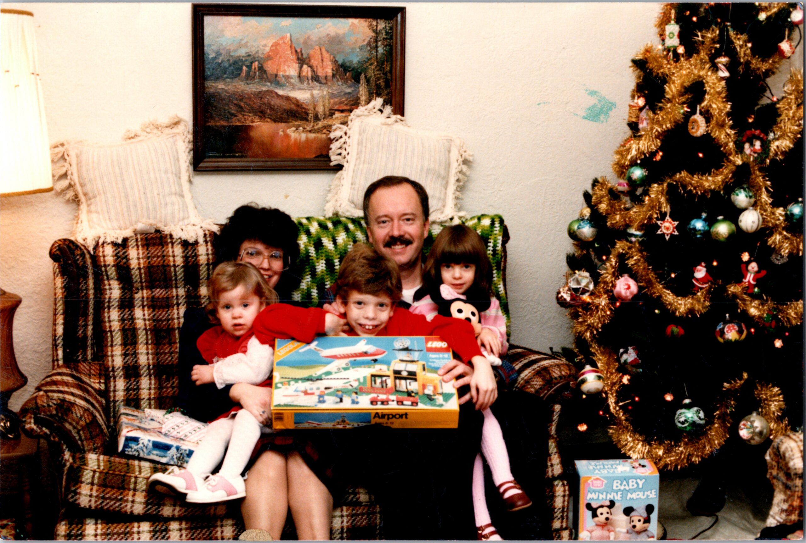 Family gathered on a plaid couch with Christmas gifts and a decorated tree in a cozy living room.
