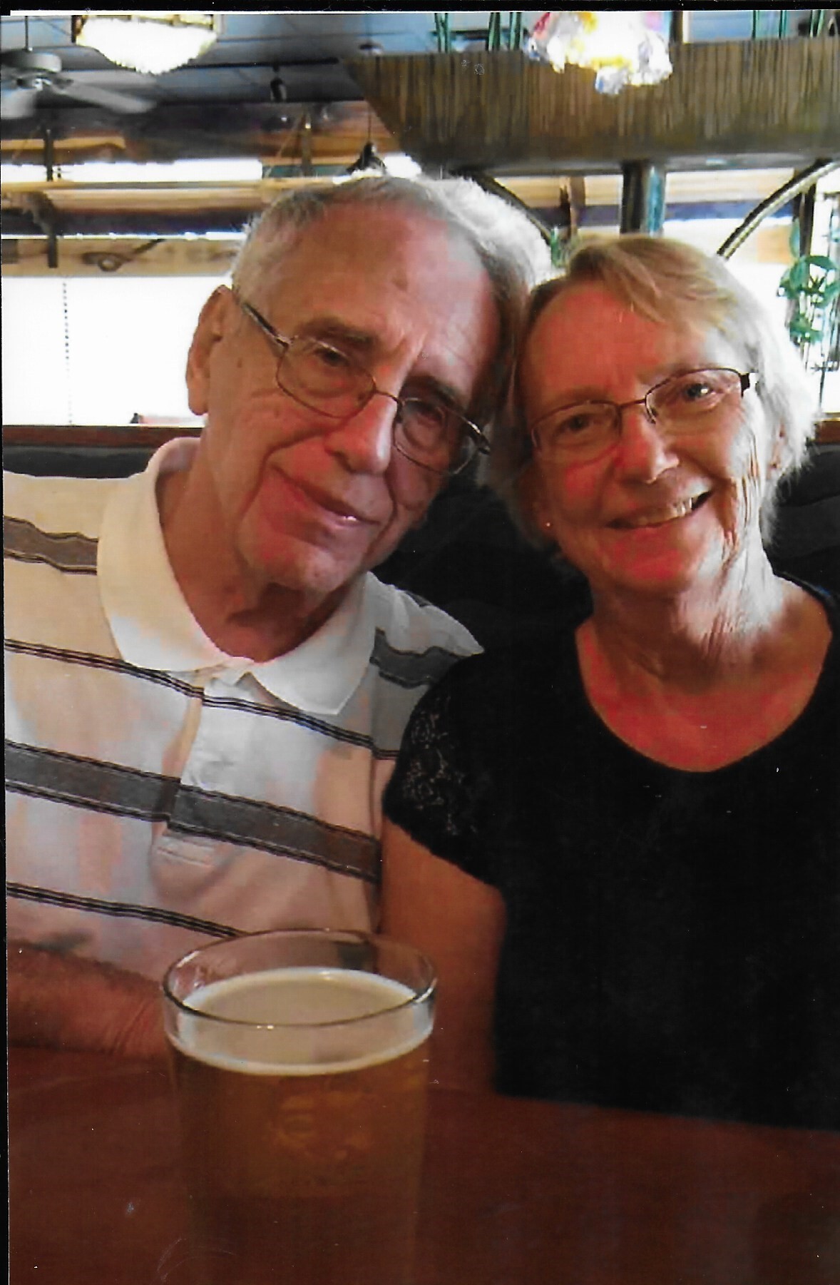 Older couple smiling at a restaurant table with a frothy beer in the foreground.